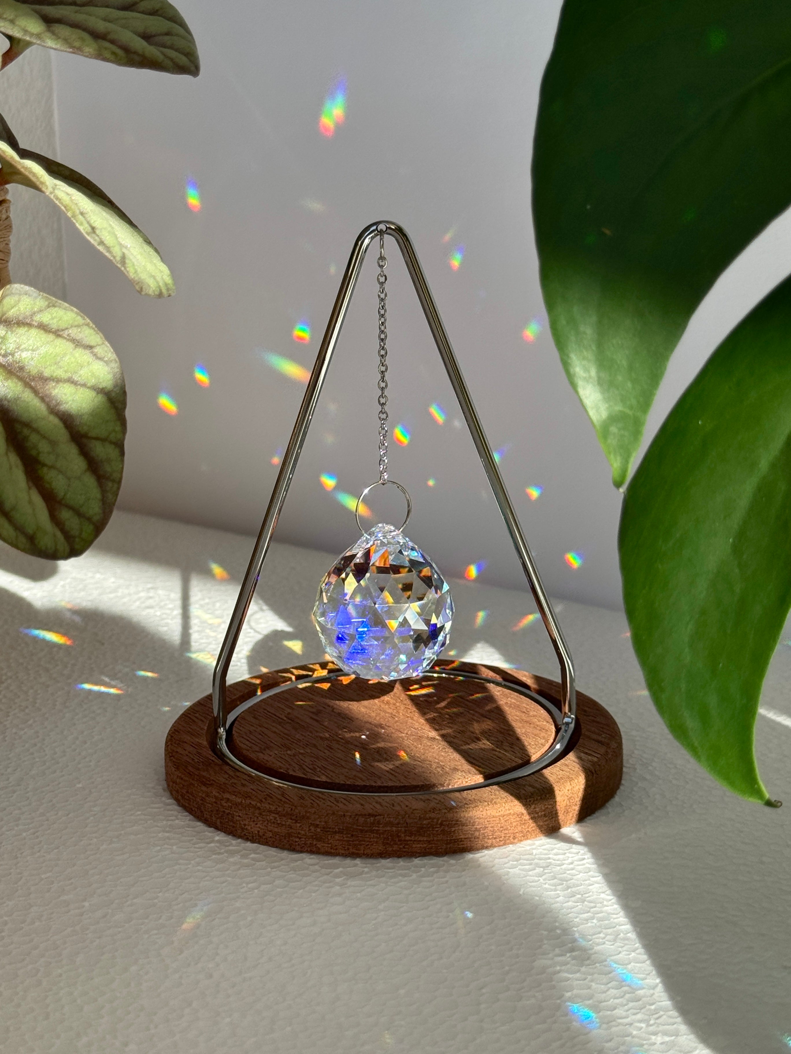 A standing tabletop suncatcher with metal triangle and hanging crystal prism surrounded by plants