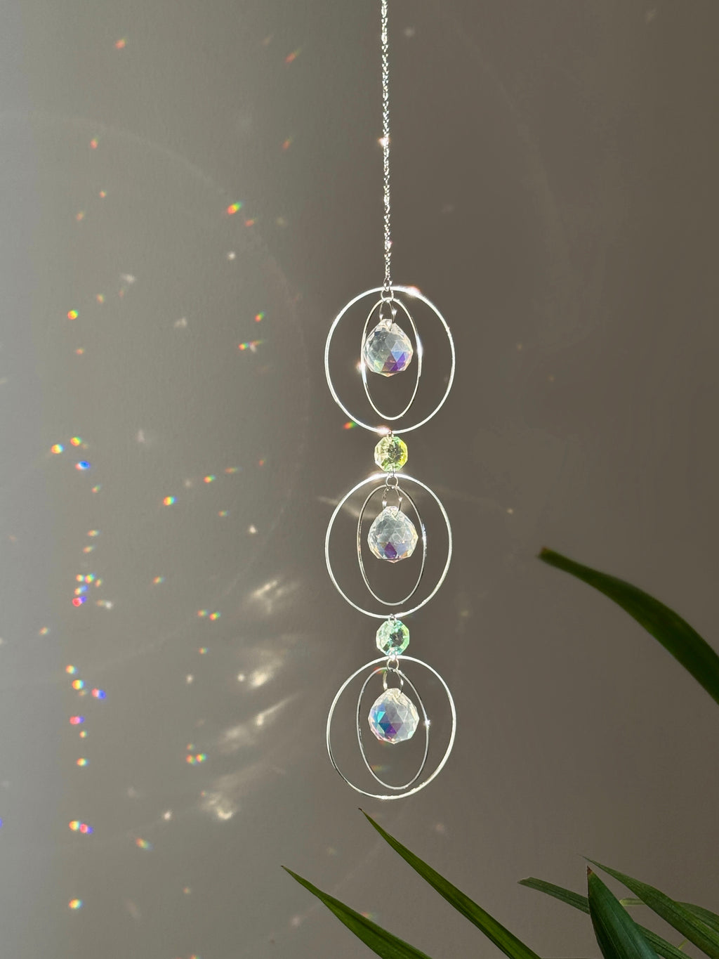 A silver-toned triple-tiered suncatcher made of stainless steel hoops. Each of the three orbits holds a clear crystal sphere with an AB coating, reflecting iridescent rainbow colors against a neutral background.