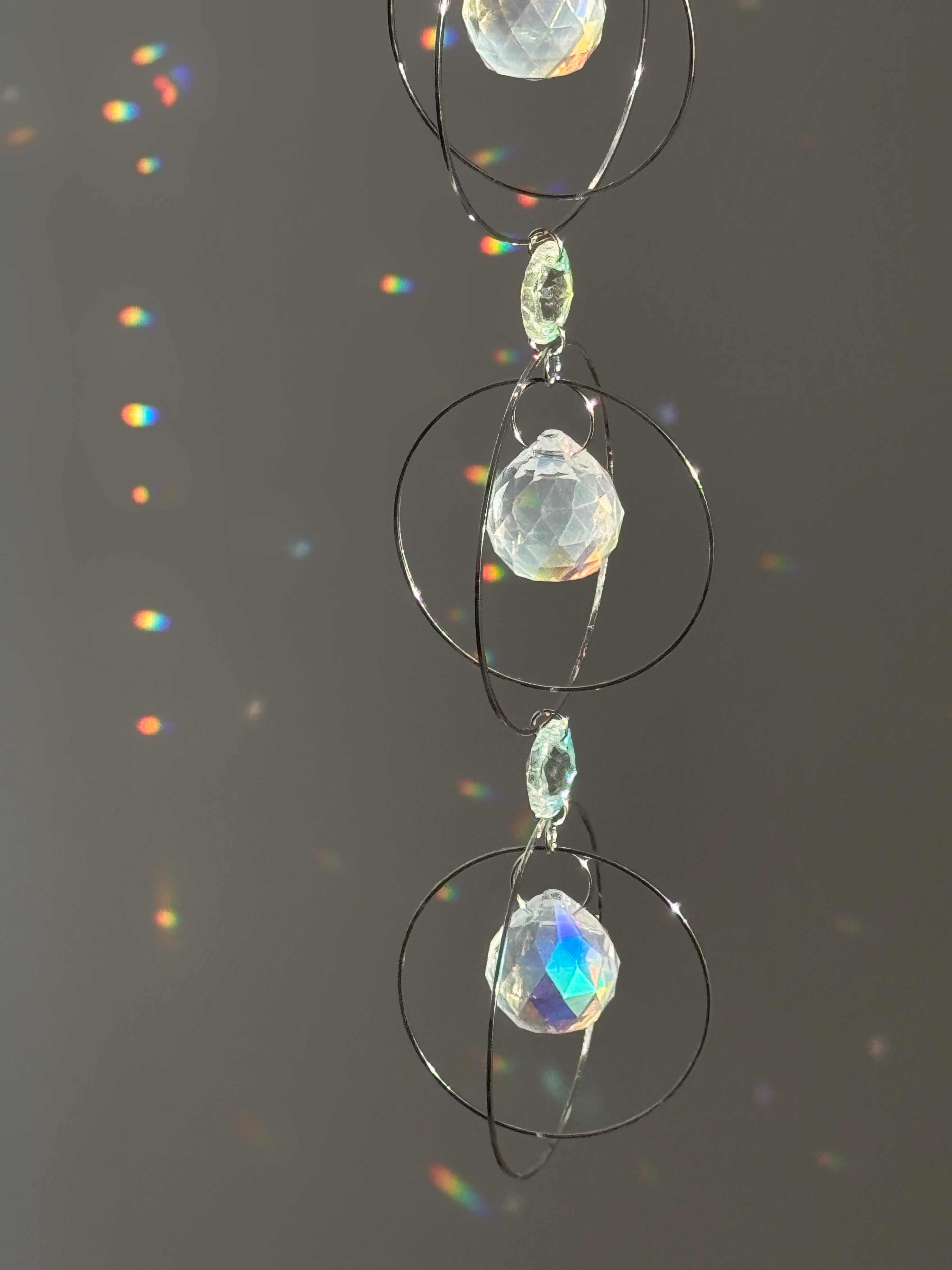 A silver-toned triple-tiered suncatcher made of stainless steel hoops. Each of the three orbits holds a clear crystal sphere with an AB coating, reflecting iridescent rainbow colors against a neutral background.