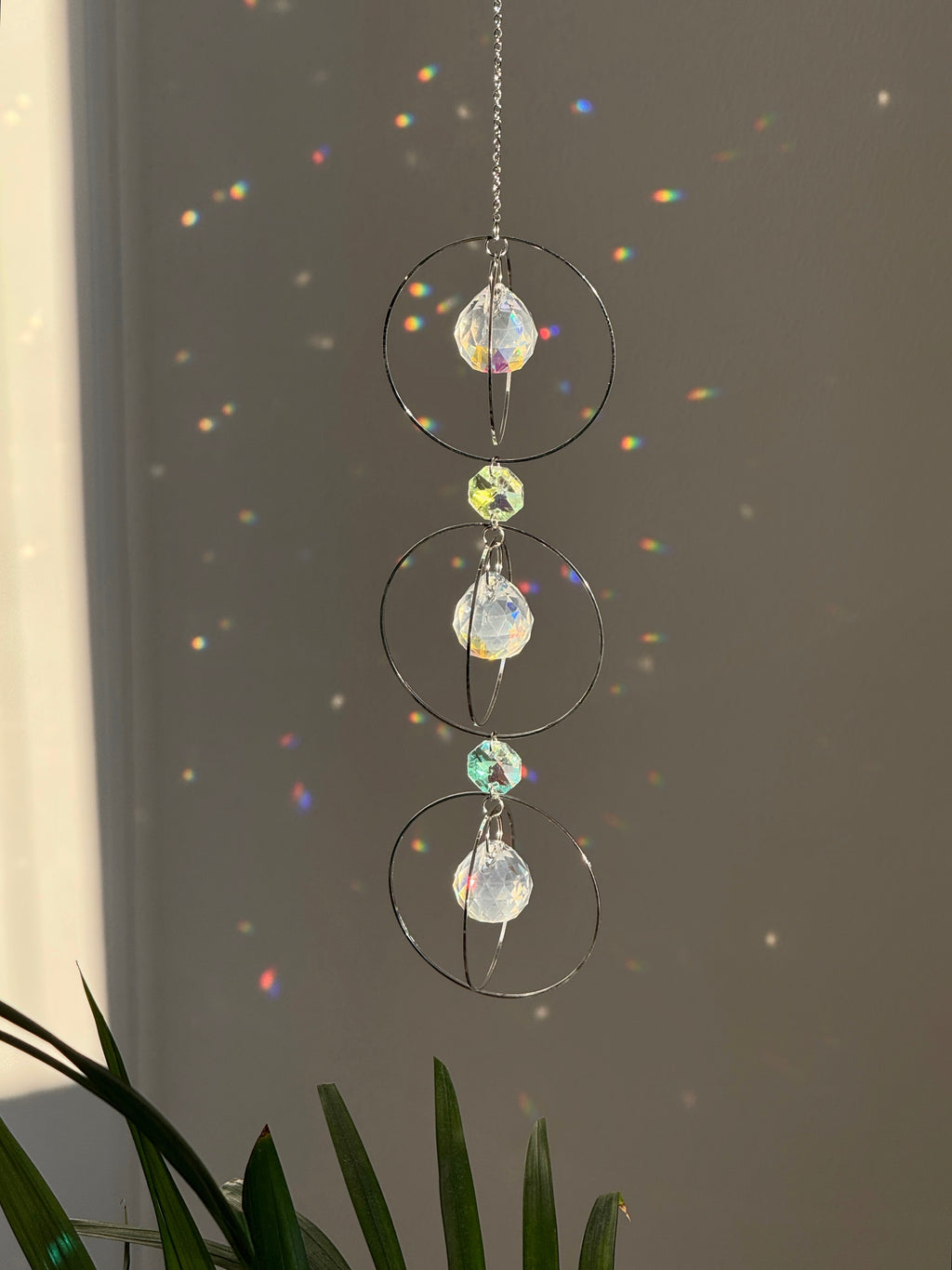 A silver-toned triple-tiered suncatcher made of stainless steel hoops. Each of the three orbits holds a clear crystal sphere with an AB coating, reflecting iridescent rainbow colors against a neutral background.