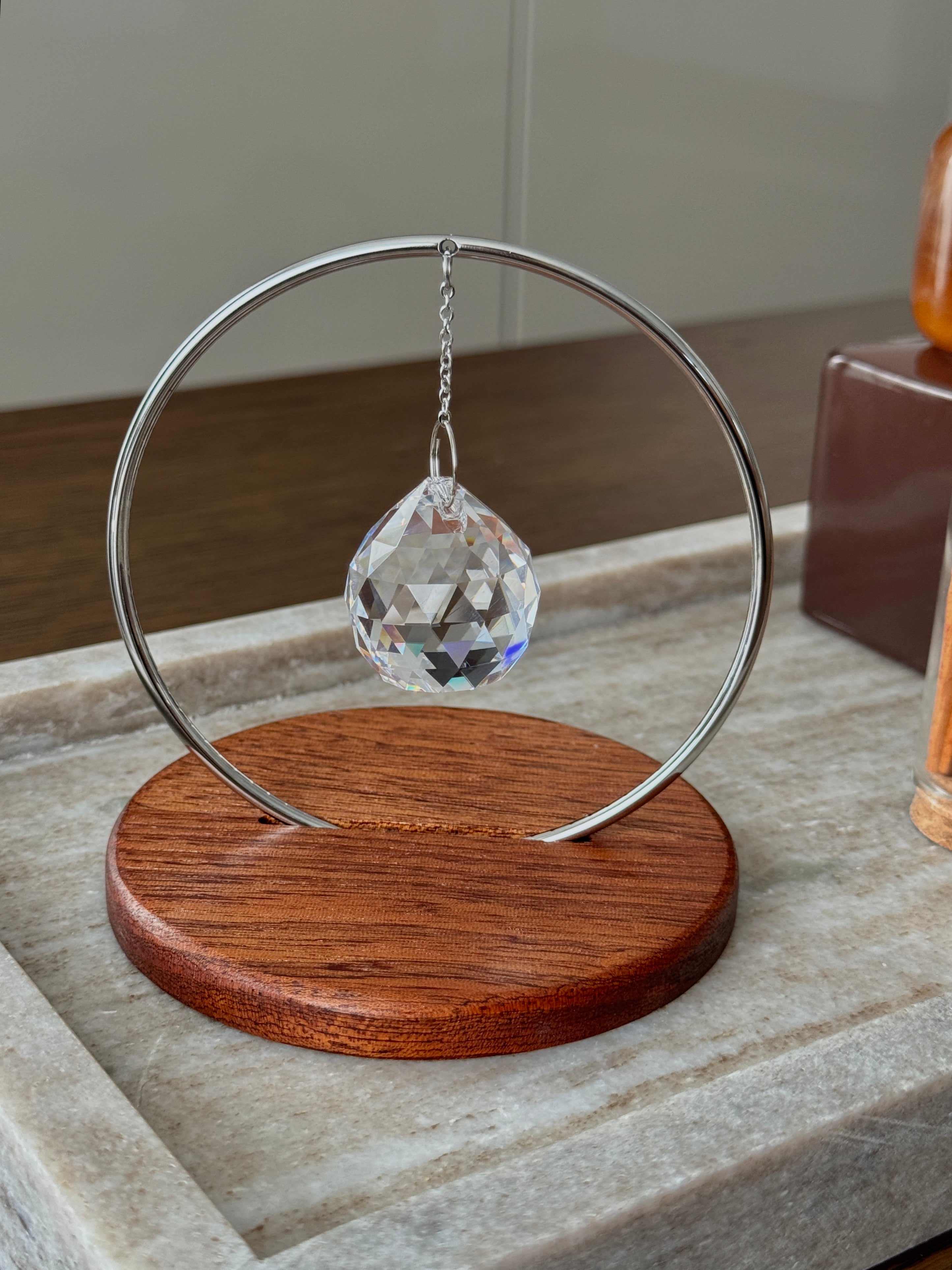 The Circle tabletop suncatcher featuring a silver stainless steel ring and faceted crystal prism casting vibrant rainbows on a white surface.