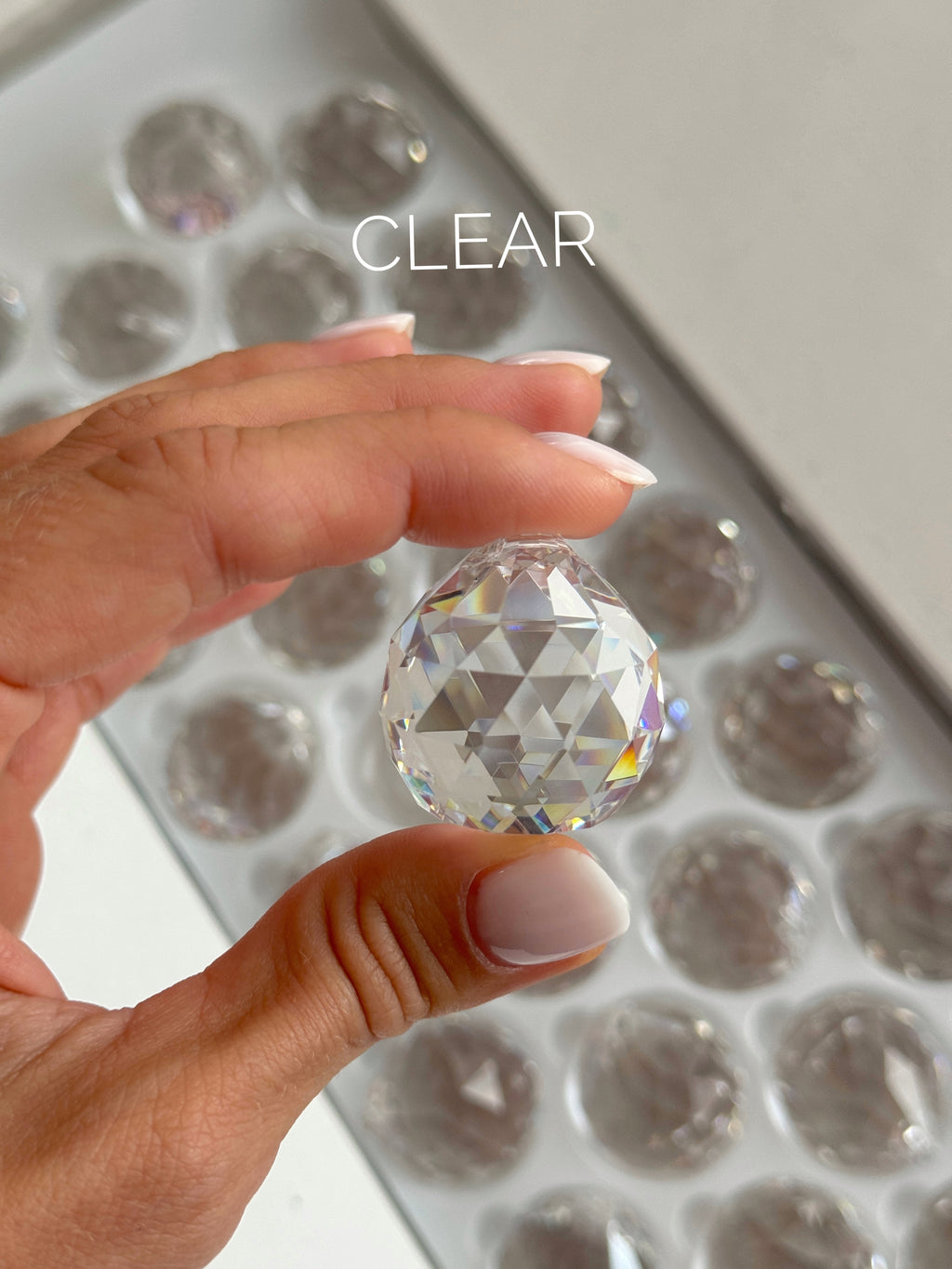 Clear crystal ball held by a hand with a tray of similar crystals in the background.