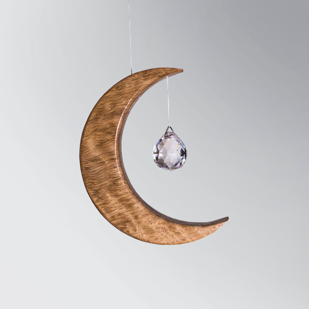 Signature Crescent Mond Sonnenfänger: Handcrafted Oak Wood Moon with 4cm Asfour Kristallprisma hanging in sunlight.