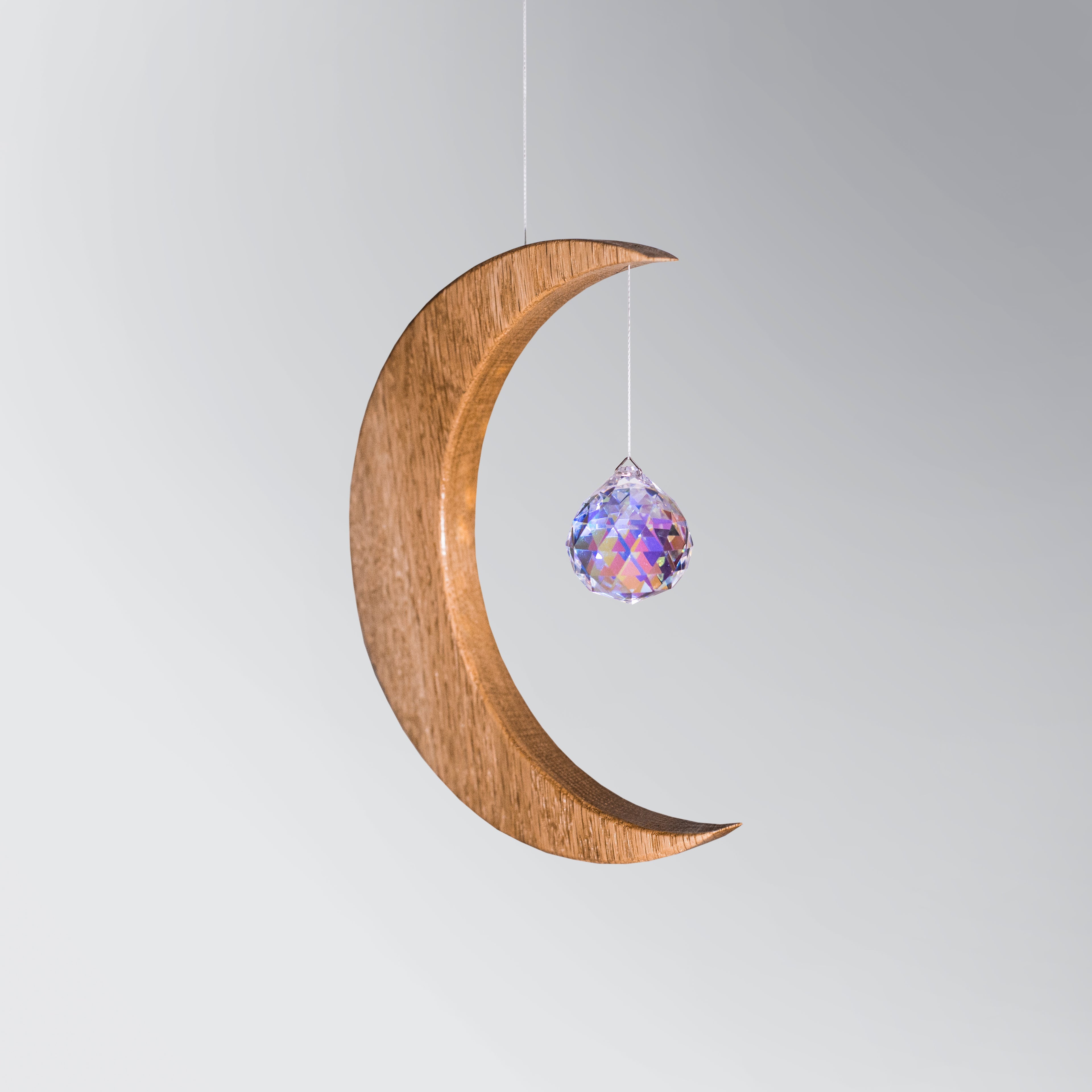 Signature Crescent Mond Sonnenfänger: Handcrafted Oak Wood Moon with 4cm Asfour Kristallprisma hanging in sunlight.