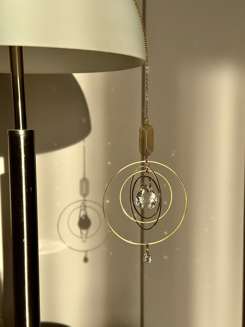 Golden boho suncatcher (Fensterdeko) hanging near an indoor lamp, showing how the crystal prism (Kristall) creates soft light reflections even in low evening light.