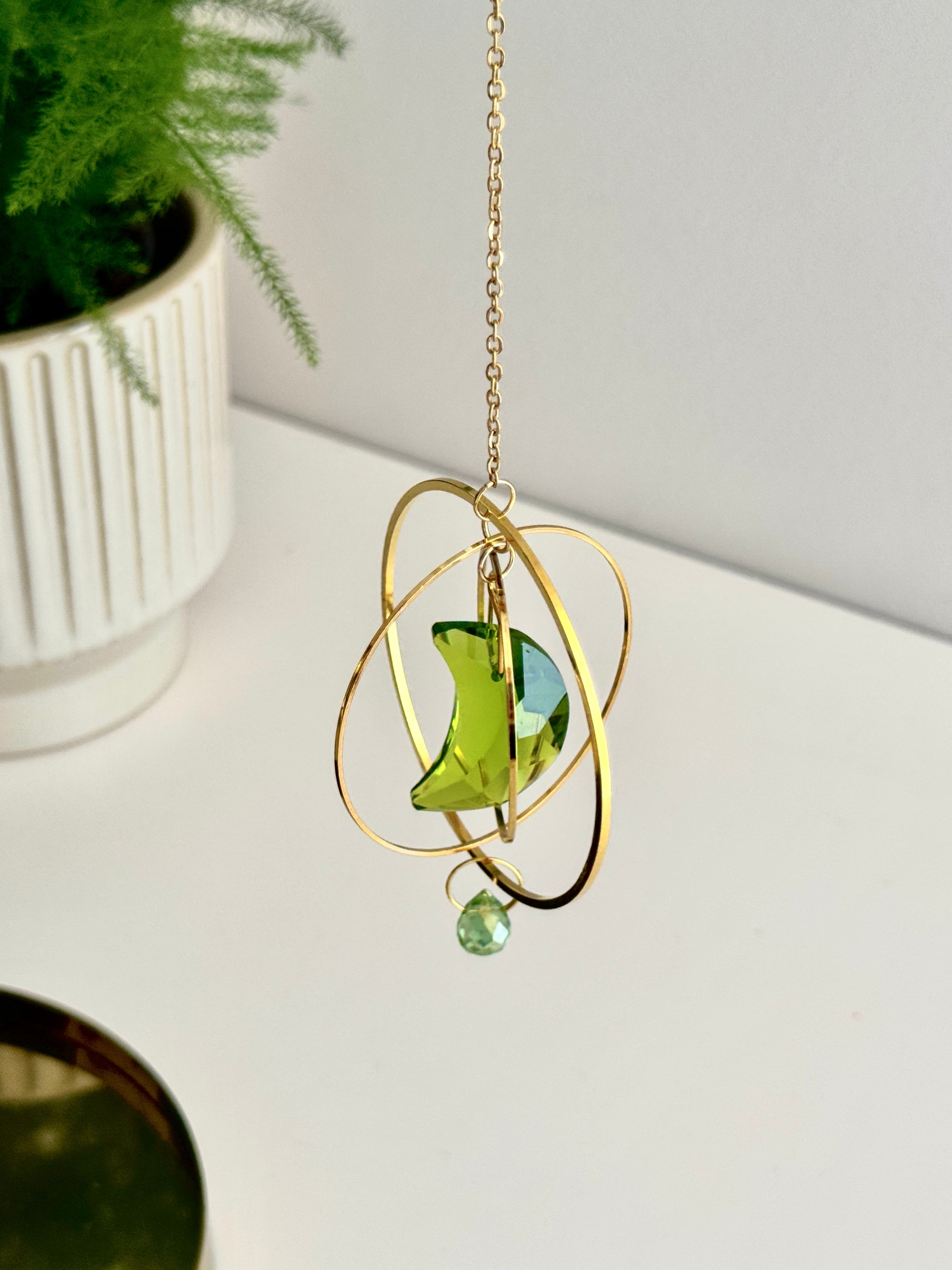 Handmade green crescent moon crystal suncatcher "Over the Moon" casting magical rainbows on a wall. Celestial gold ring window decor and rainbow maker (Sonnenfänger)