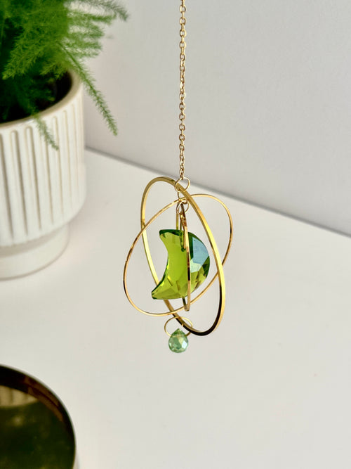 Handmade green crescent moon crystal suncatcher "Over the Moon" casting magical rainbows on a wall. Celestial gold ring window decor and rainbow maker (Sonnenfänger)