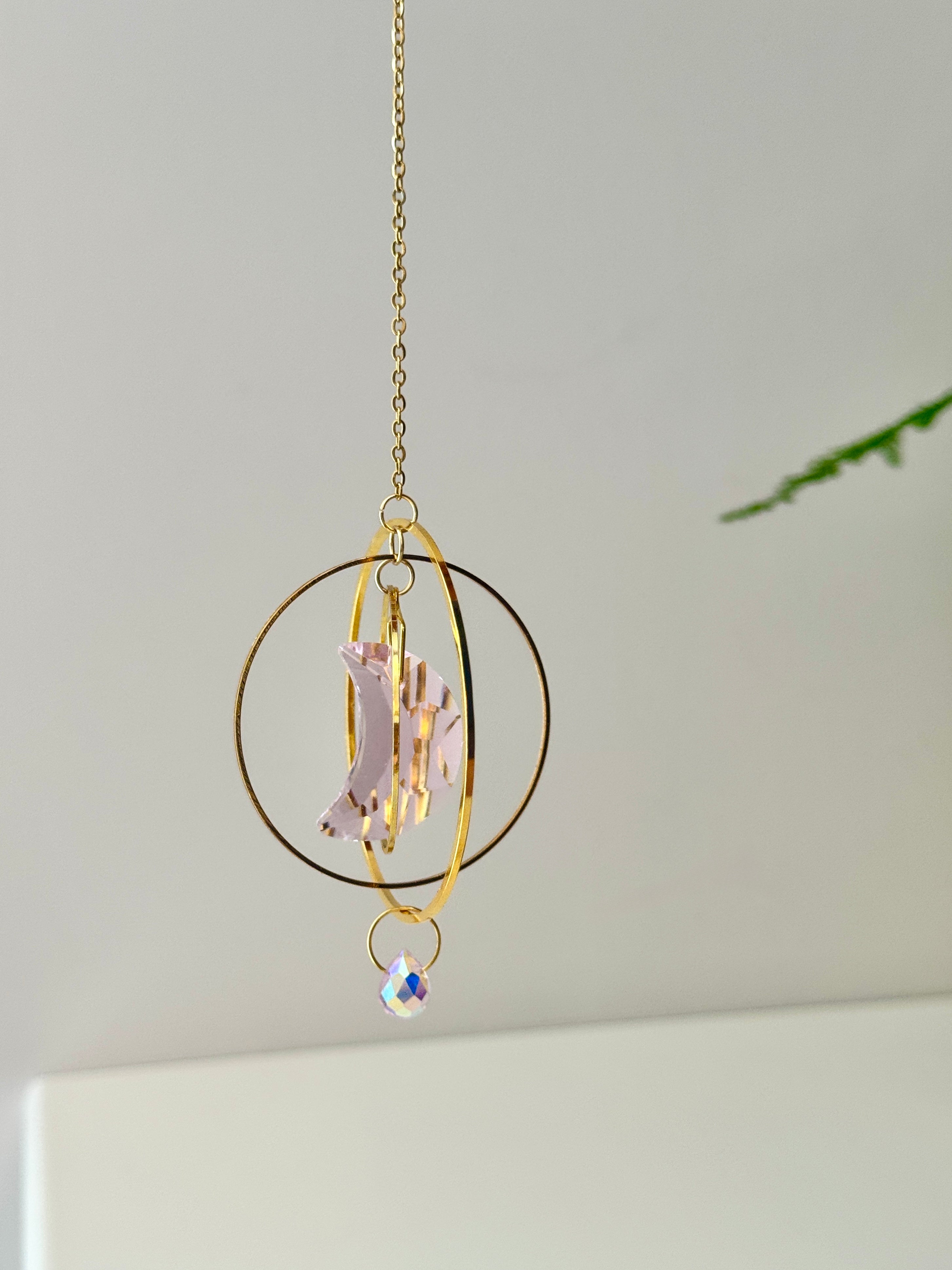 Handmade pink crescent moon suncatcher hanging in a sunny window creating rainbow prisms on the wall