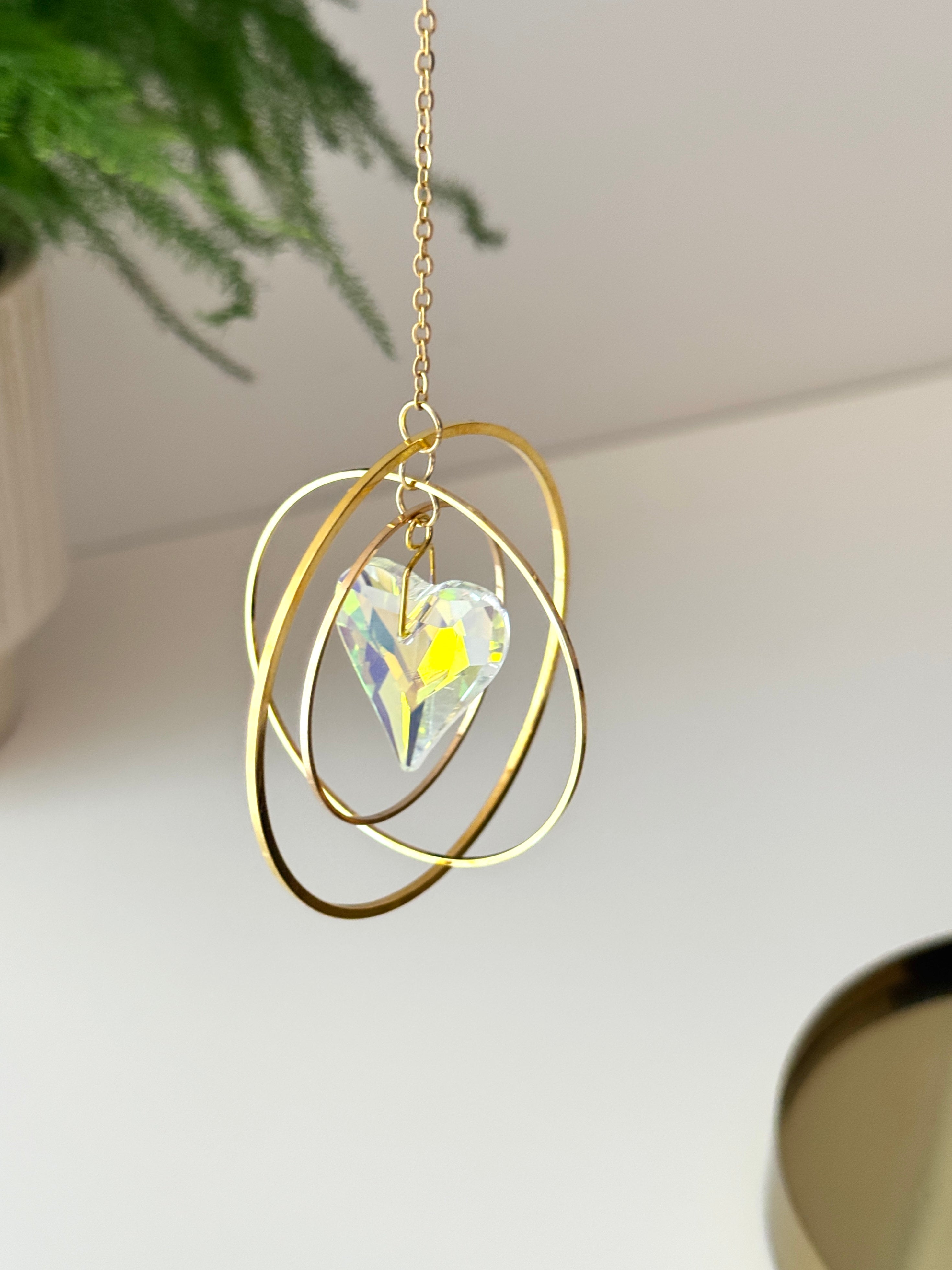 Handcrafted Sunkissed Heartbeat suncatcher with a faceted crystal heart and gold rings casting vibrant rainbows on a white wall.