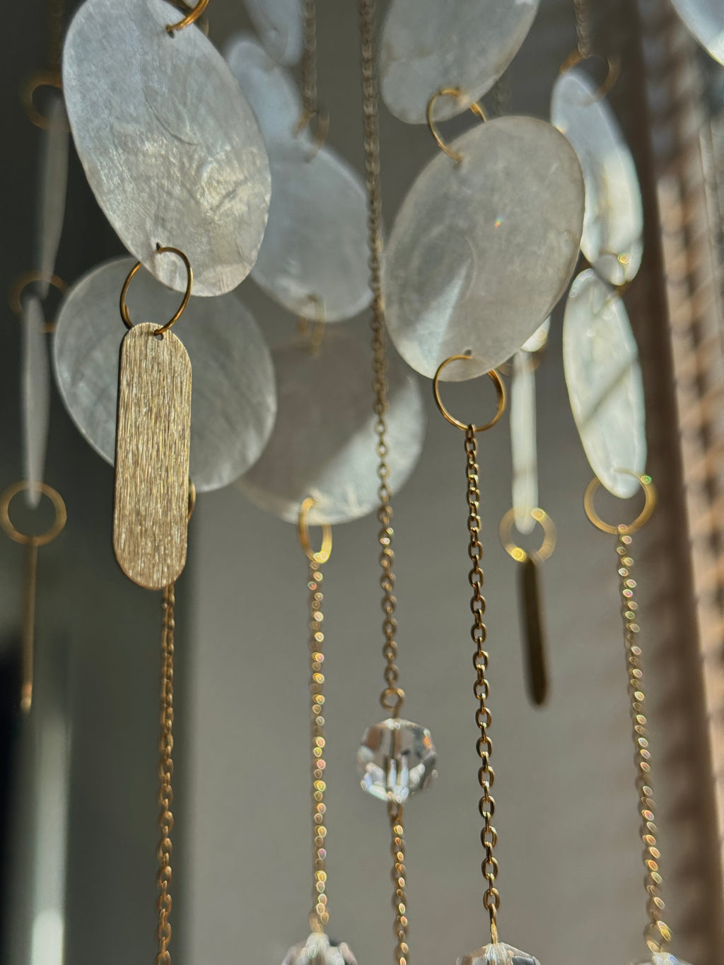 A close-up of a hanging decorative wall art piece with translucent oval discs, gold-tone rings, chains, and clear faceted crystal pendants.