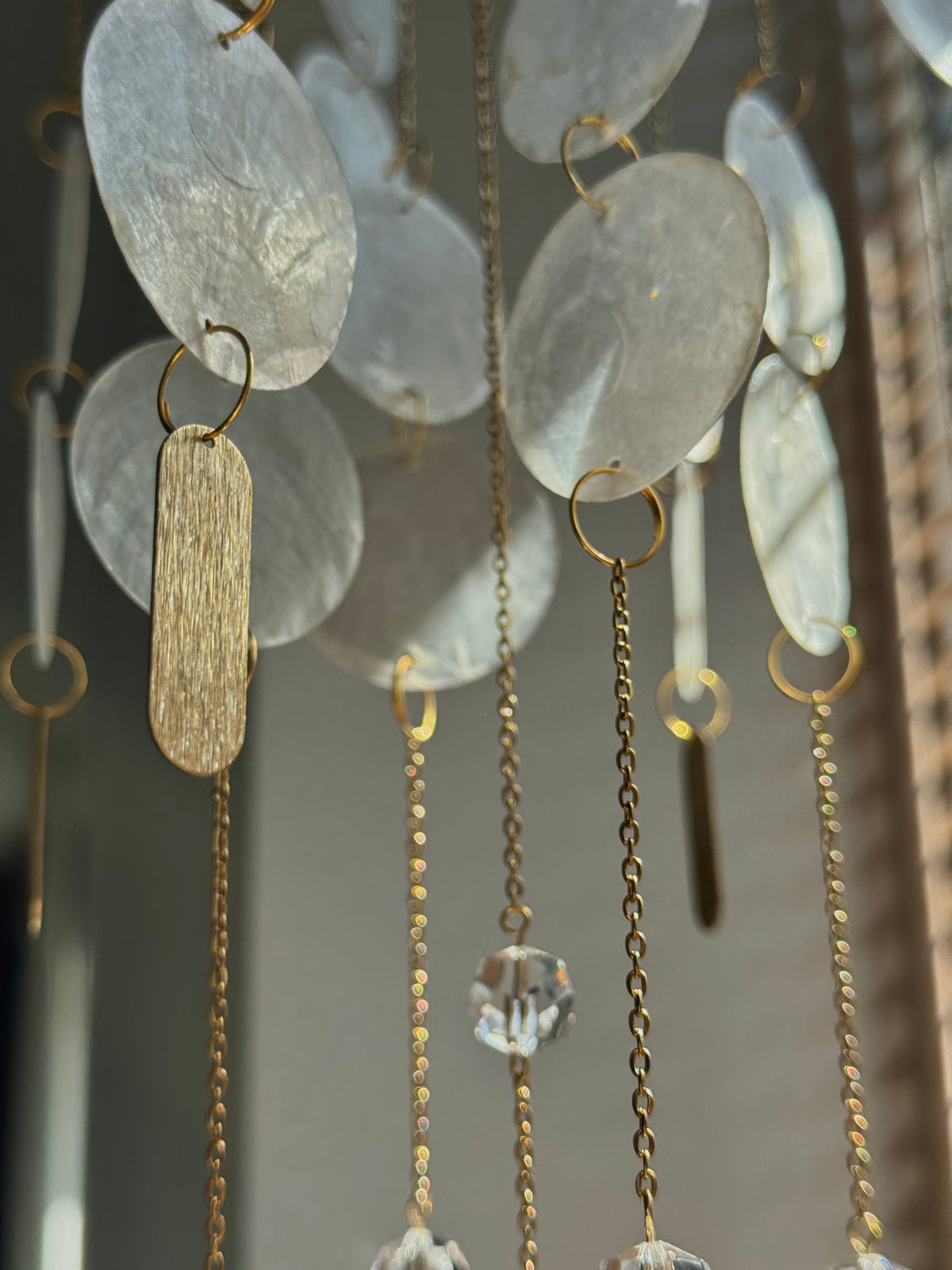 A close-up of a hanging decorative wall art piece with translucent oval discs, gold-tone rings, chains, and clear faceted crystal pendants.