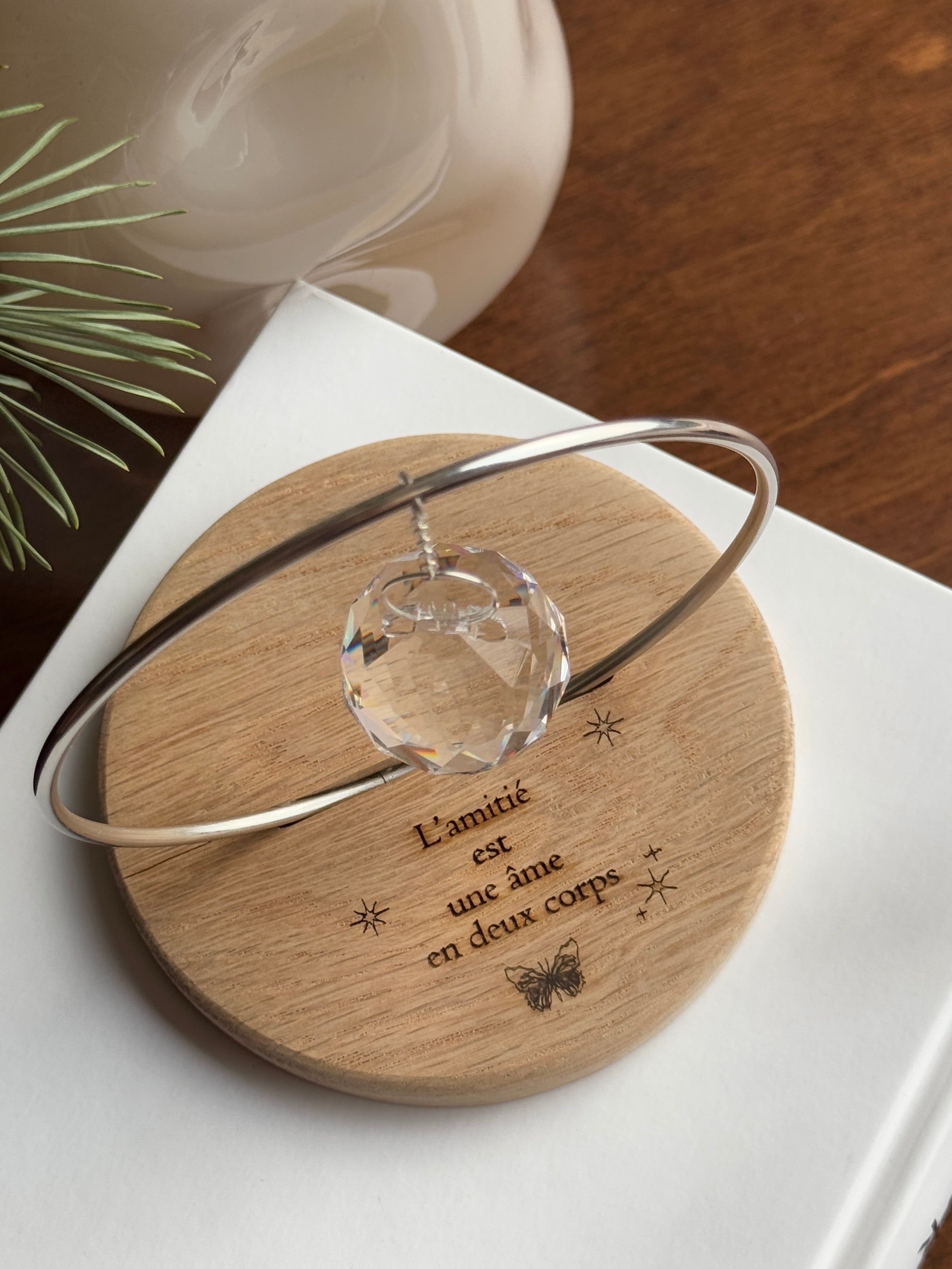 The Circle - A minimalist Sonnenfänger (suncatcher) featuring a high-quality faceted Kristall-Prisma suspended by a delicate gold stainless steel chain within a matching gold ring. The modern tabletop design rests on a solid, dark redwood base (Echtholz-Sockel) and is shown creating vibrant rainbow light reflections (Regenbogen-Effekt) across the background. This elegant Fensterdeko is perfect as a mindful Geschenkidee for home or office.