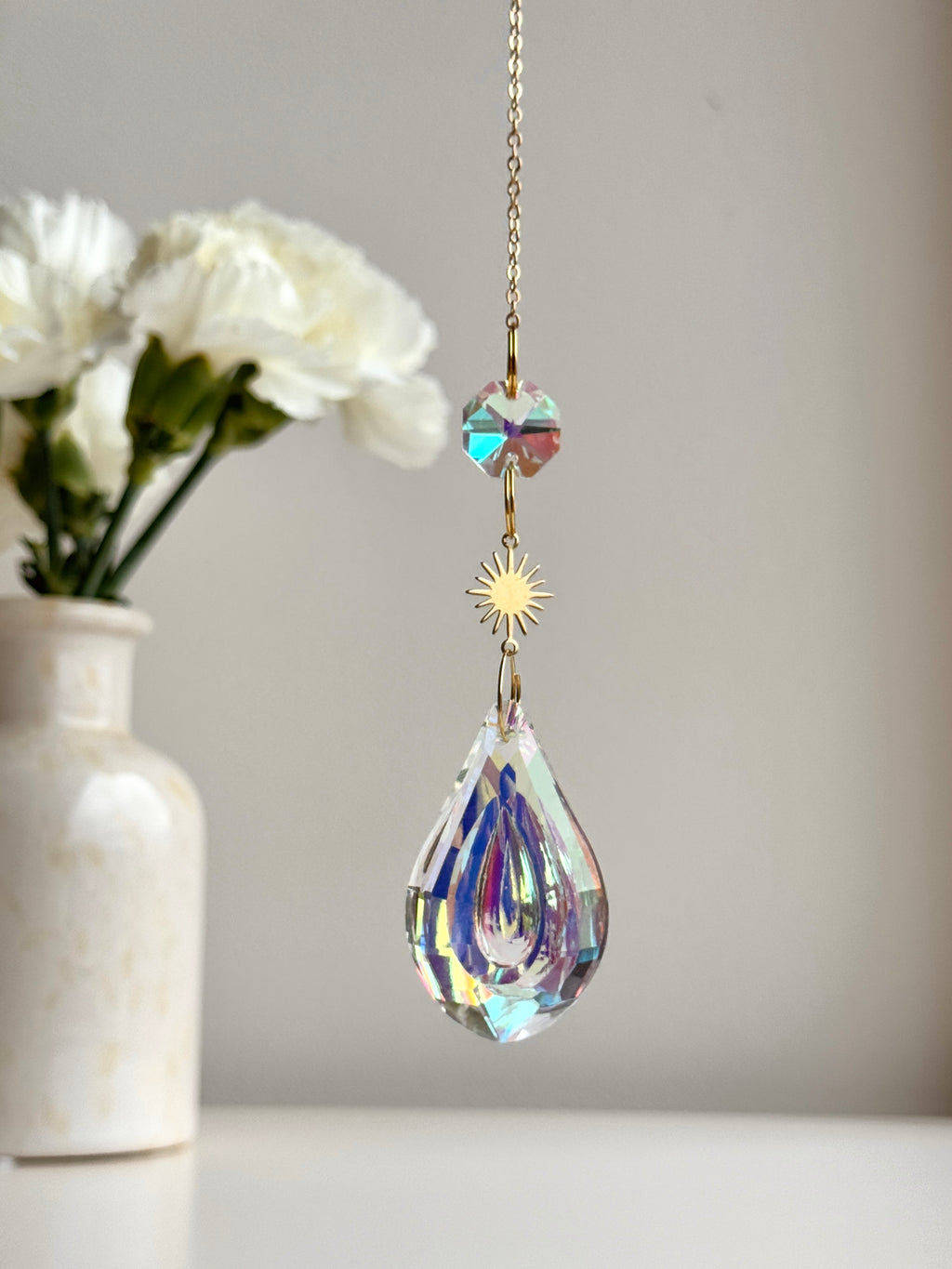 Celestial Droplet suncatcher (Sonnenfänger) with a 4cm teardrop crystal prism reflecting vibrant rainbows (Regenbogen) on a bright interior wall.