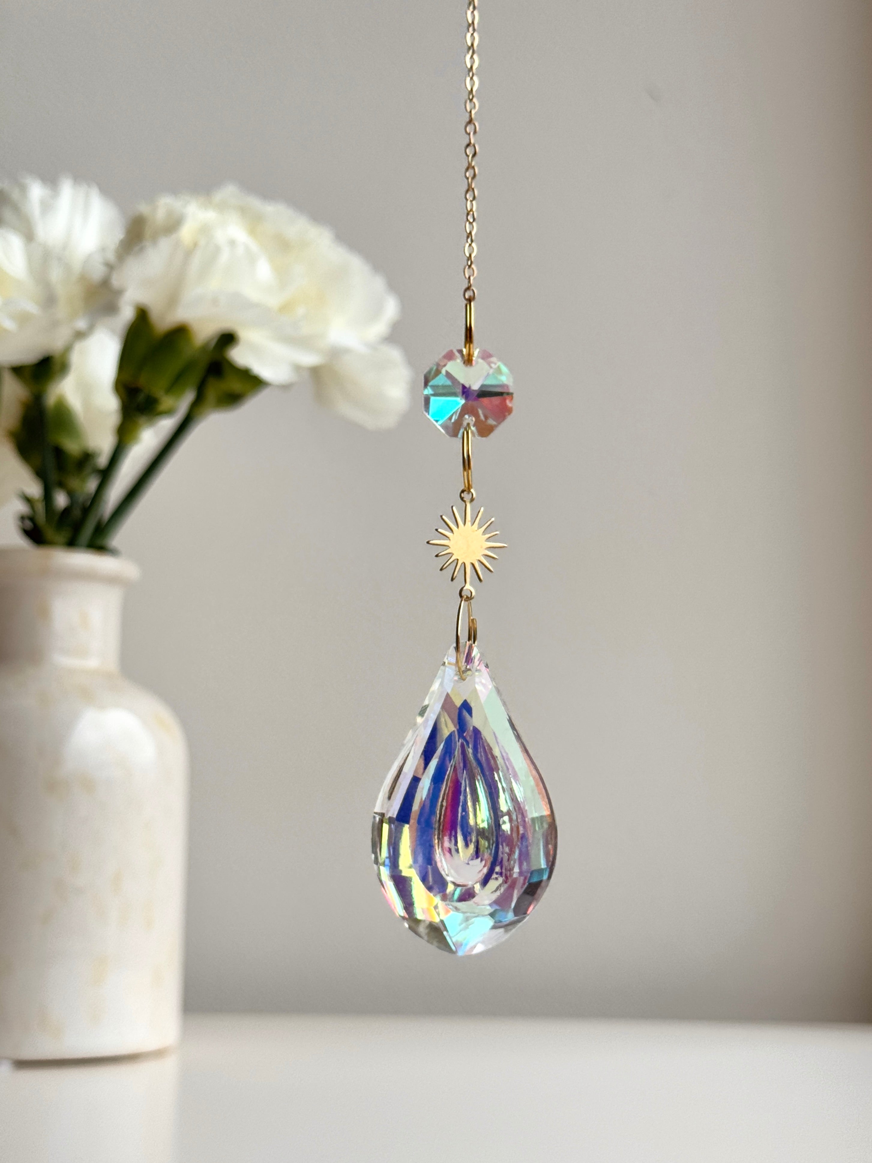Celestial Droplet suncatcher (Sonnenfänger) with a 4cm teardrop crystal prism reflecting vibrant rainbows (Regenbogen) on a bright interior wall.