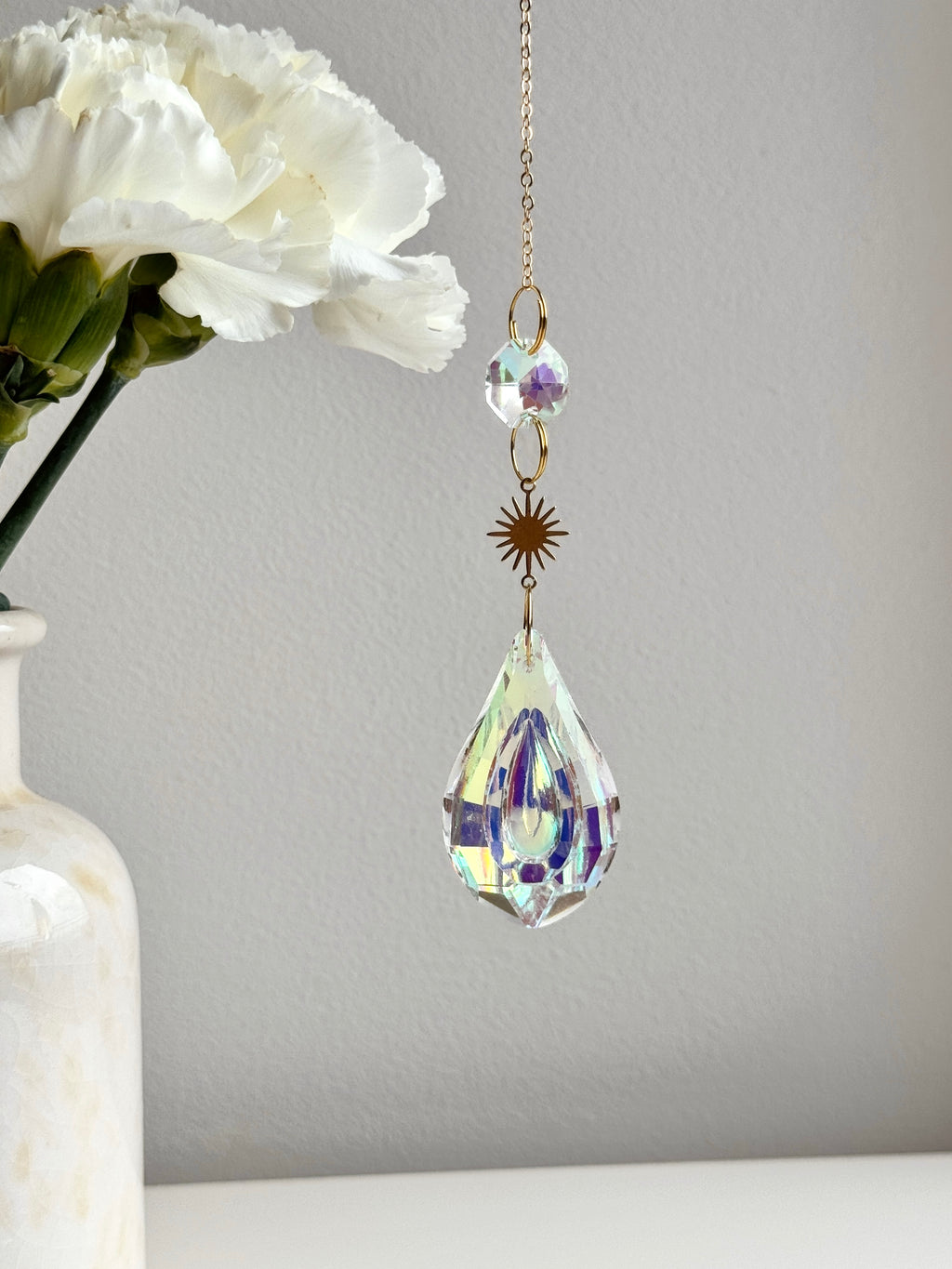 Celestial Droplet suncatcher (Sonnenfänger) with a 4cm teardrop crystal prism reflecting vibrant rainbows (Regenbogen) on a bright interior wall.