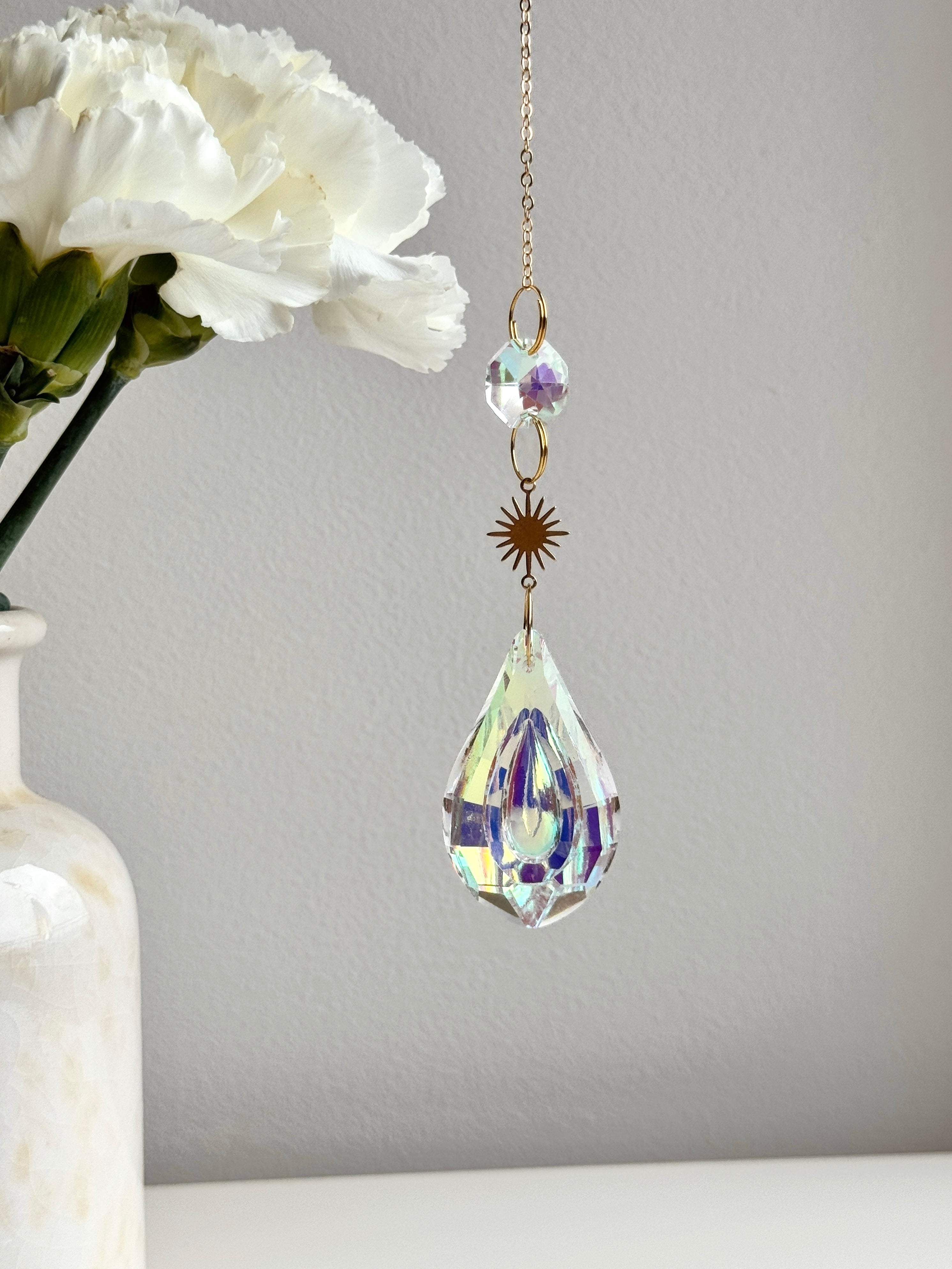 Celestial Droplet suncatcher (Sonnenfänger) with a 4cm teardrop crystal prism reflecting vibrant rainbows (Regenbogen) on a bright interior wall.