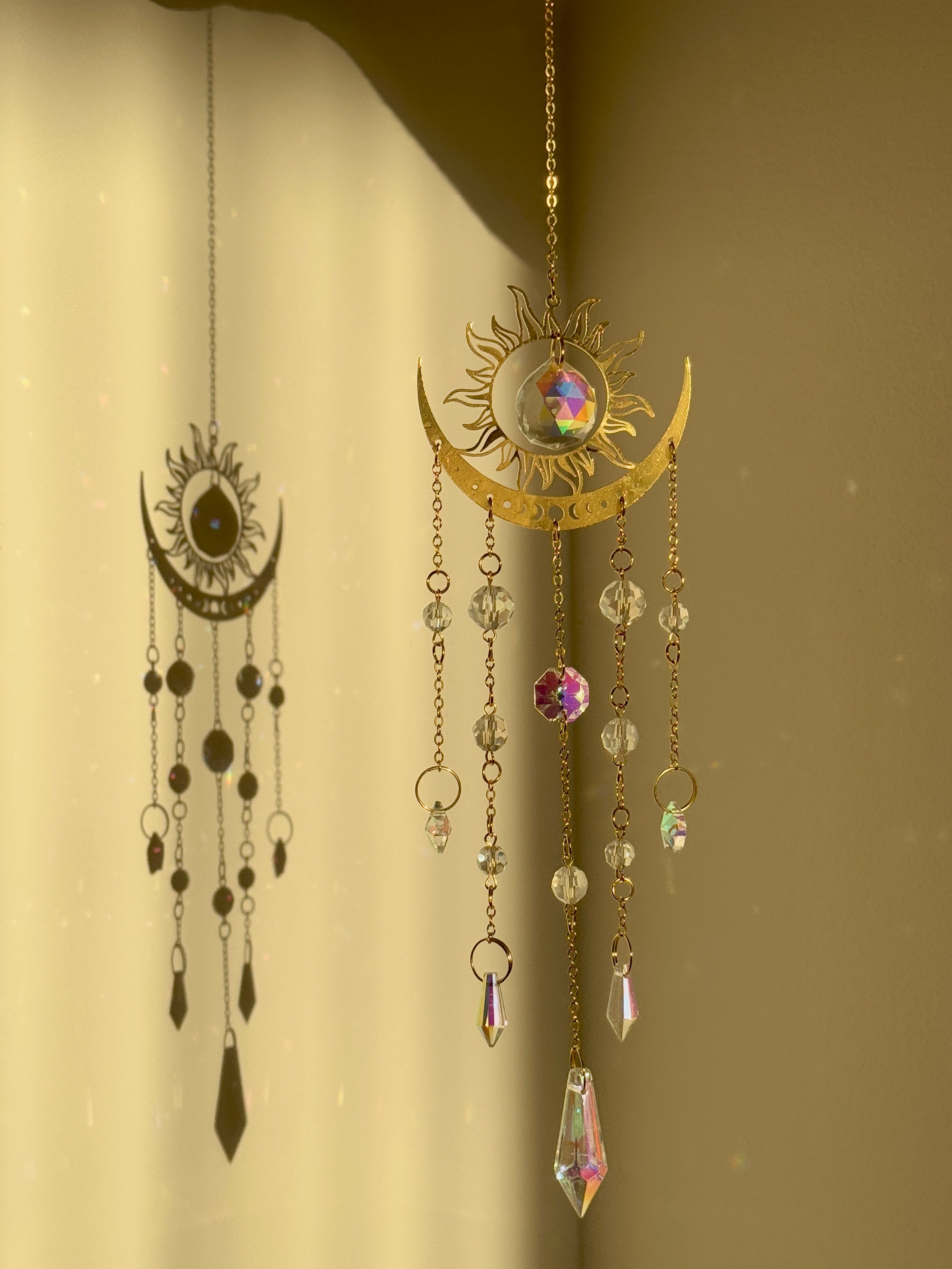 The Aura suncatcher featuring a gold crescent moon and sunburst with hanging crystal stars and prisms. Handgefertigter Sonnenfänger casting vivid rainbows on the wall. Boho-Stil Fensterdeko and magical Lichtreflexe home ornament.