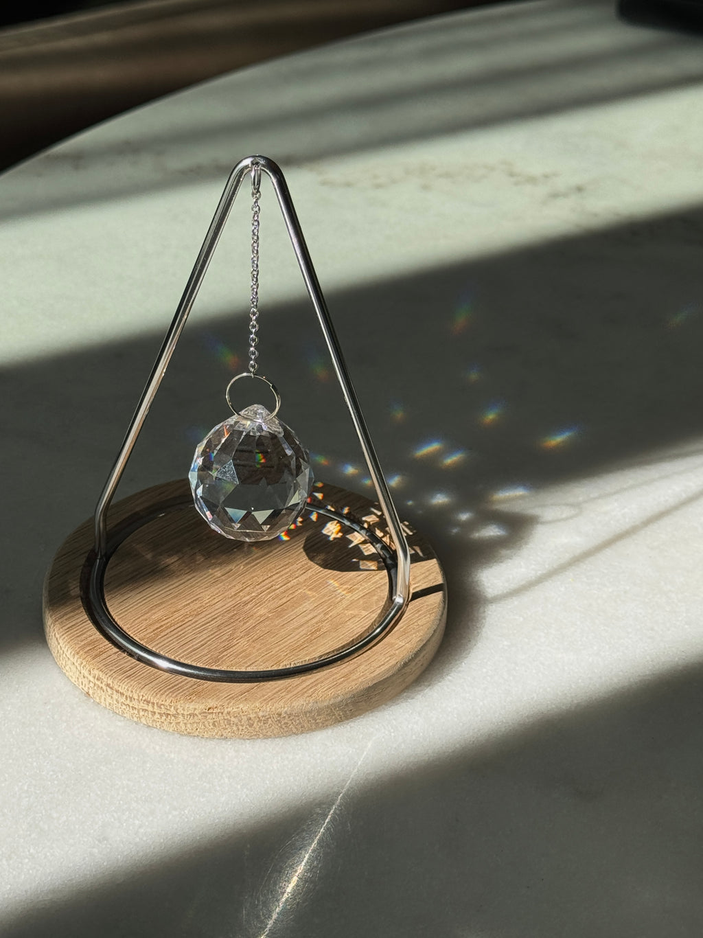 The Triangle Sonnenfänger: A modern crystal prism suncatcher with a handcrafted oak wood base and stainless steel frame, creating magical rainbow reflections.