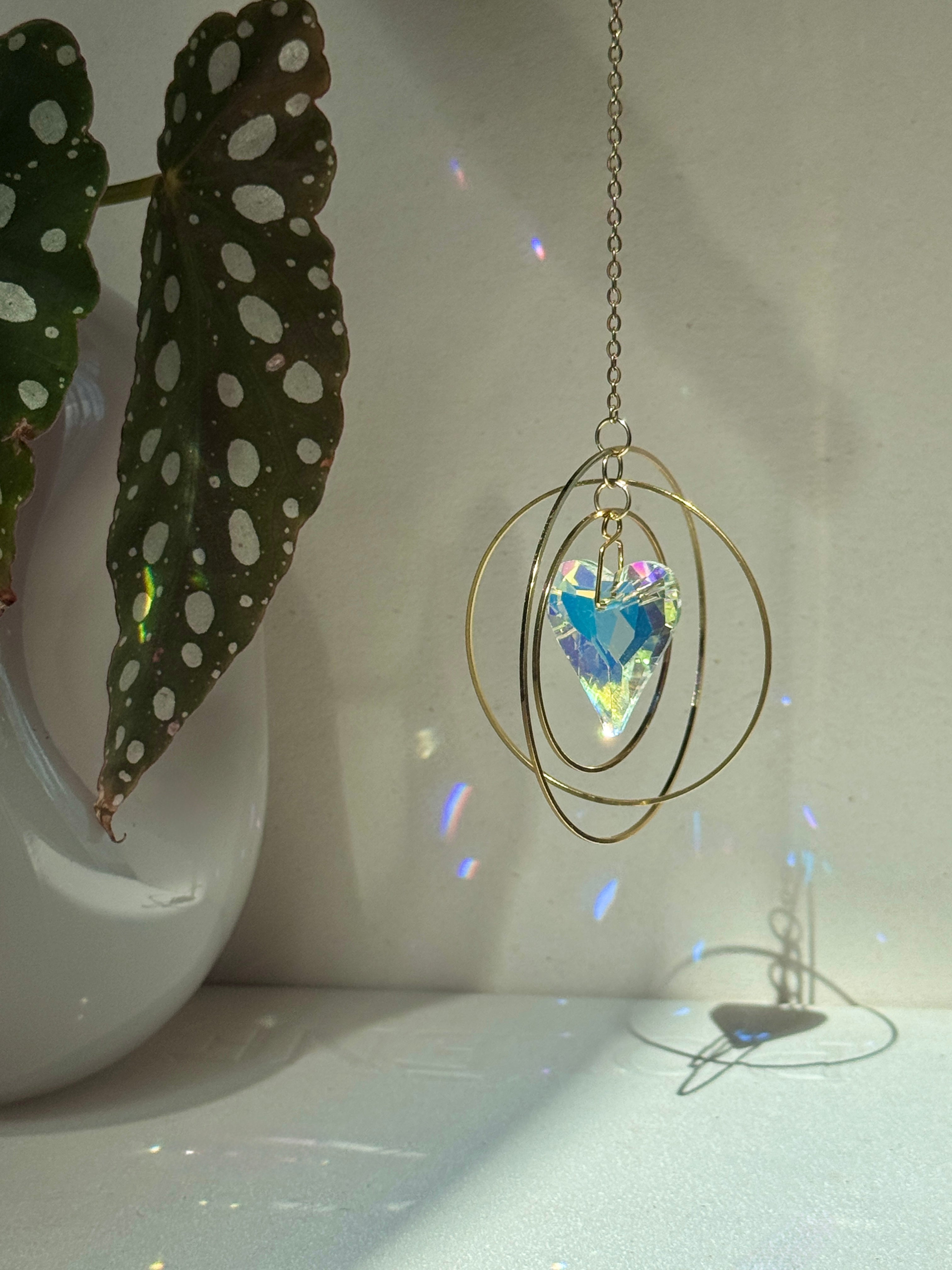 Handcrafted Sunkissed Heartbeat suncatcher with a faceted crystal heart and gold rings casting vibrant rainbows on a white wall.