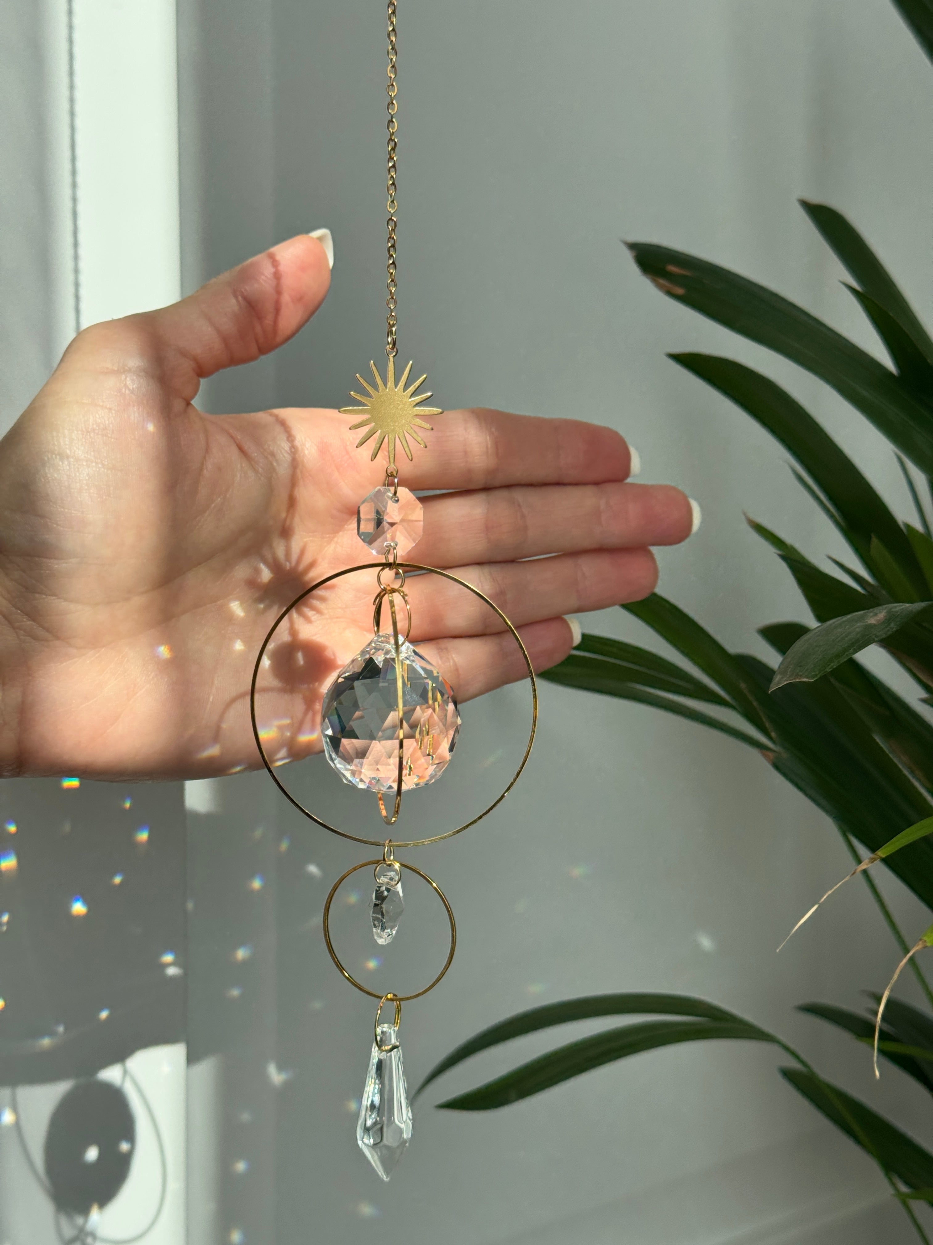 Gold celestial suncatcher with clear crystal prisms casting rainbow light reflections on a wall.