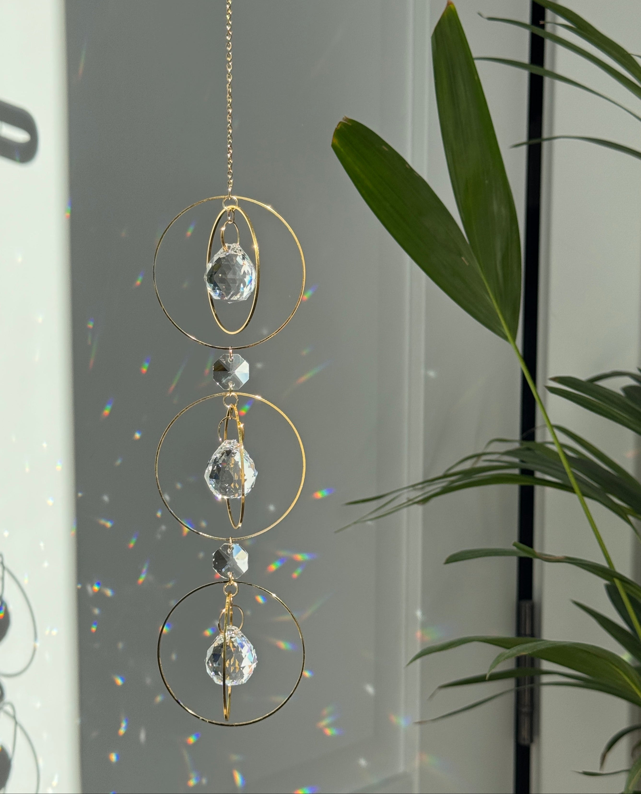 Bestselling Trinity suncatcher with triple gold circles and faceted crystals. Handgefertigter Sonnenfänger creating intense rainbow patterns on a white background. Boho-Stil window decoration and premium Lichtreflexe crystal ornament.