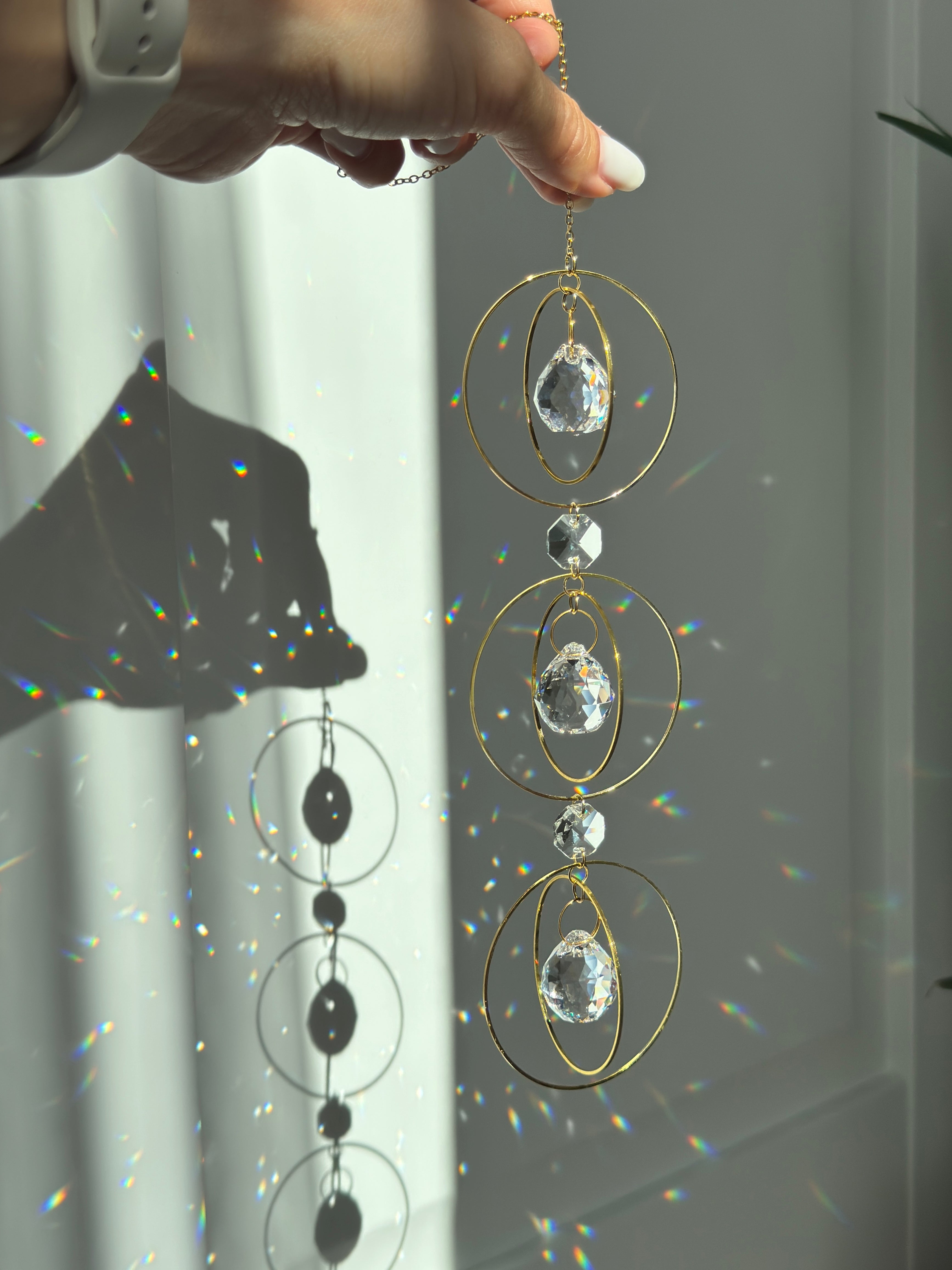 Bestselling Trinity suncatcher with triple gold circles and faceted crystals. Handgefertigter Sonnenfänger creating intense rainbow patterns on a white background. Boho-Stil window decoration and premium Lichtreflexe crystal ornament.