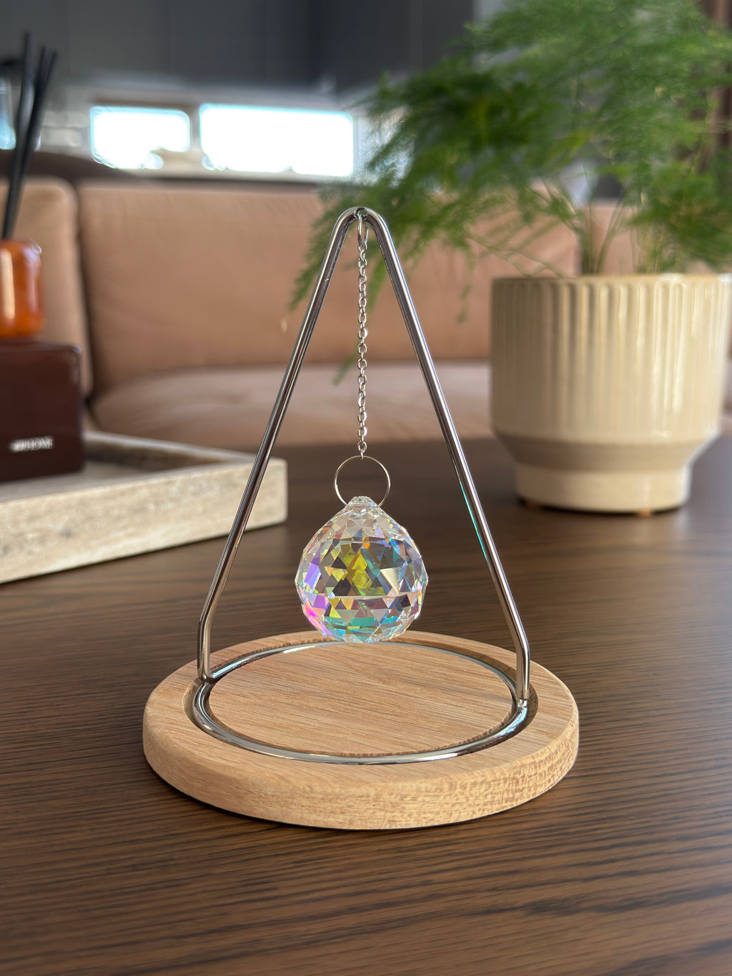 The Triangle Sonnenfänger: A modern crystal prism suncatcher with a handcrafted oak wood base and stainless steel frame, creating magical rainbow reflections.