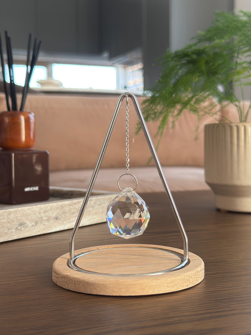 The Triangle Sonnenfänger: A modern crystal prism suncatcher with a handcrafted oak wood base and stainless steel frame, creating magical rainbow reflections.