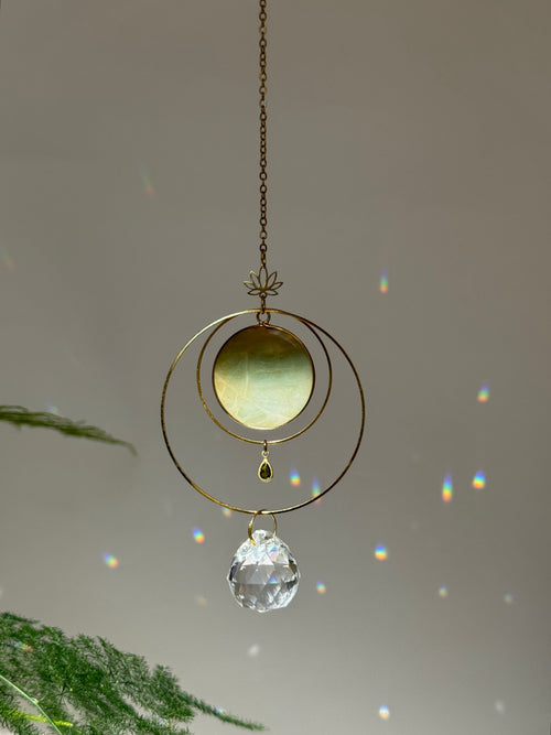 Detailed view of a gold lotus suncatcher featuring a round green Amazonite stone disc and a large faceted crystal drop reflecting rainbow light spots on a soft grey background.