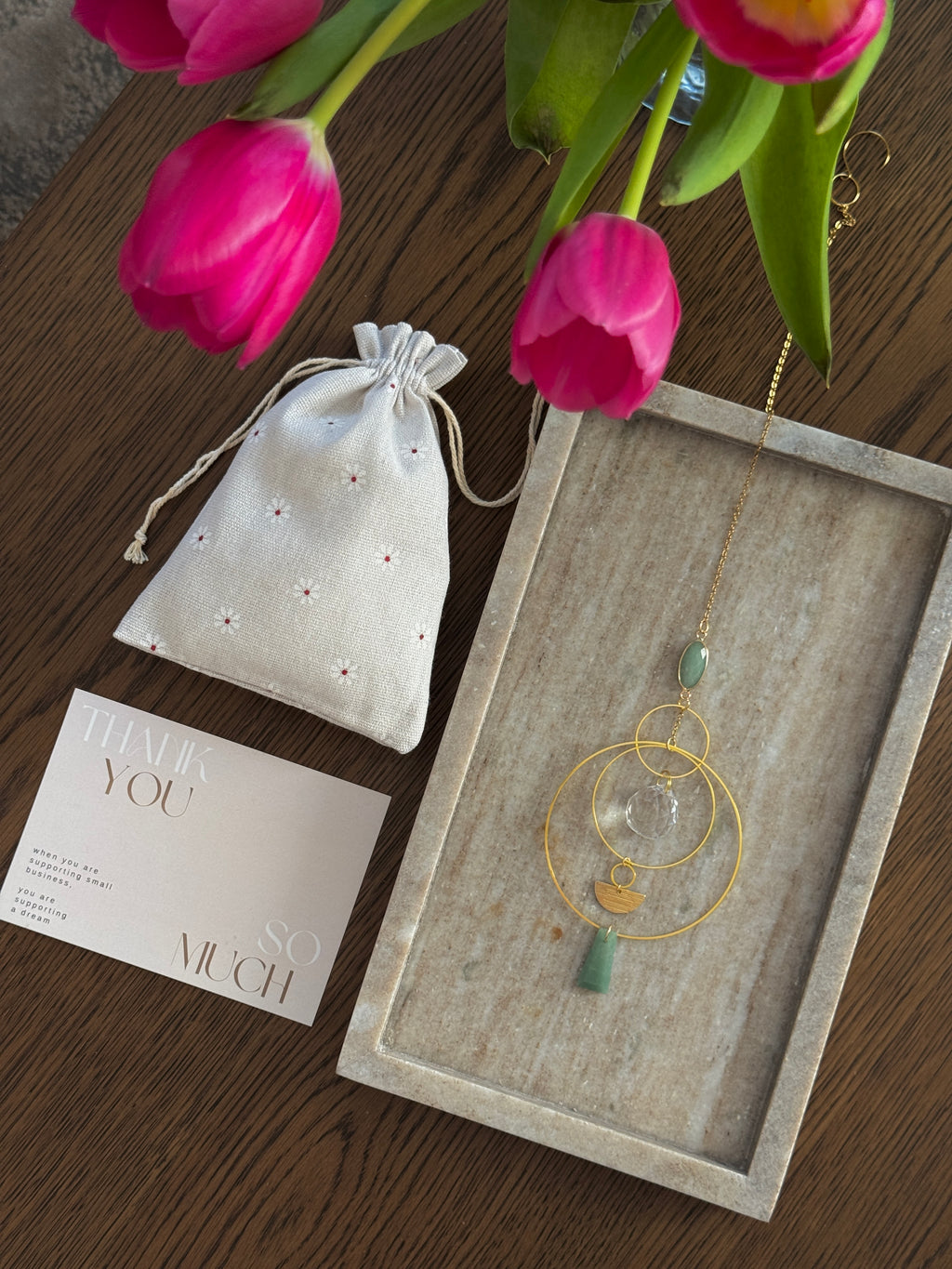 Vertical gold geometric suncatcher with three tiered hoops, a faceted crystal sphere, and two green Aventurine stones casting a galaxy of rainbows on a white wall.