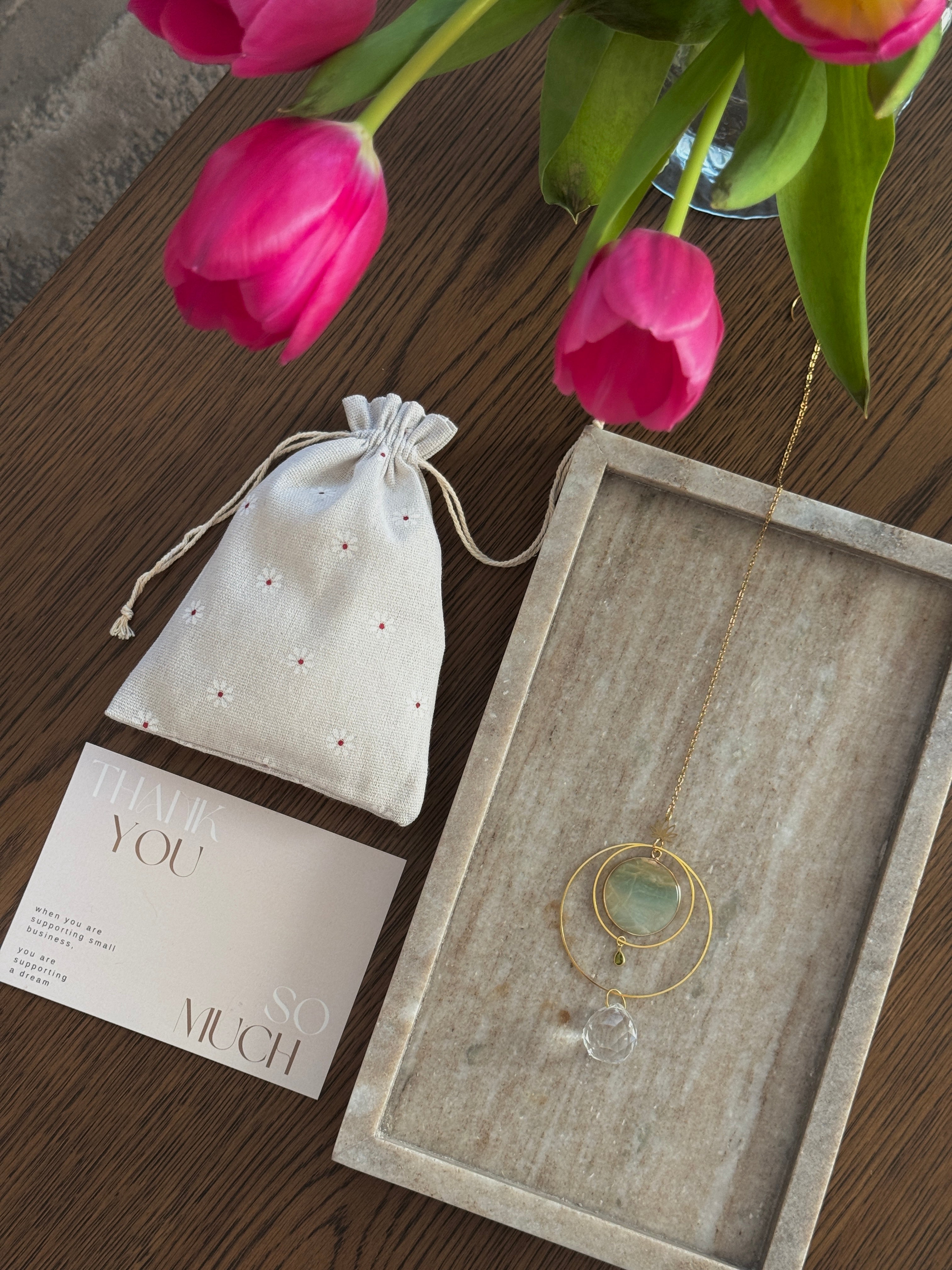 Detailed view of a gold lotus suncatcher featuring a round green Amazonite stone disc and a large faceted crystal drop reflecting rainbow light spots on a soft grey background.