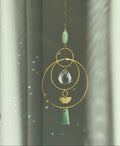 Decorative hanging ornament with gold chain, green stones, and crystal-like center against a neutral background
