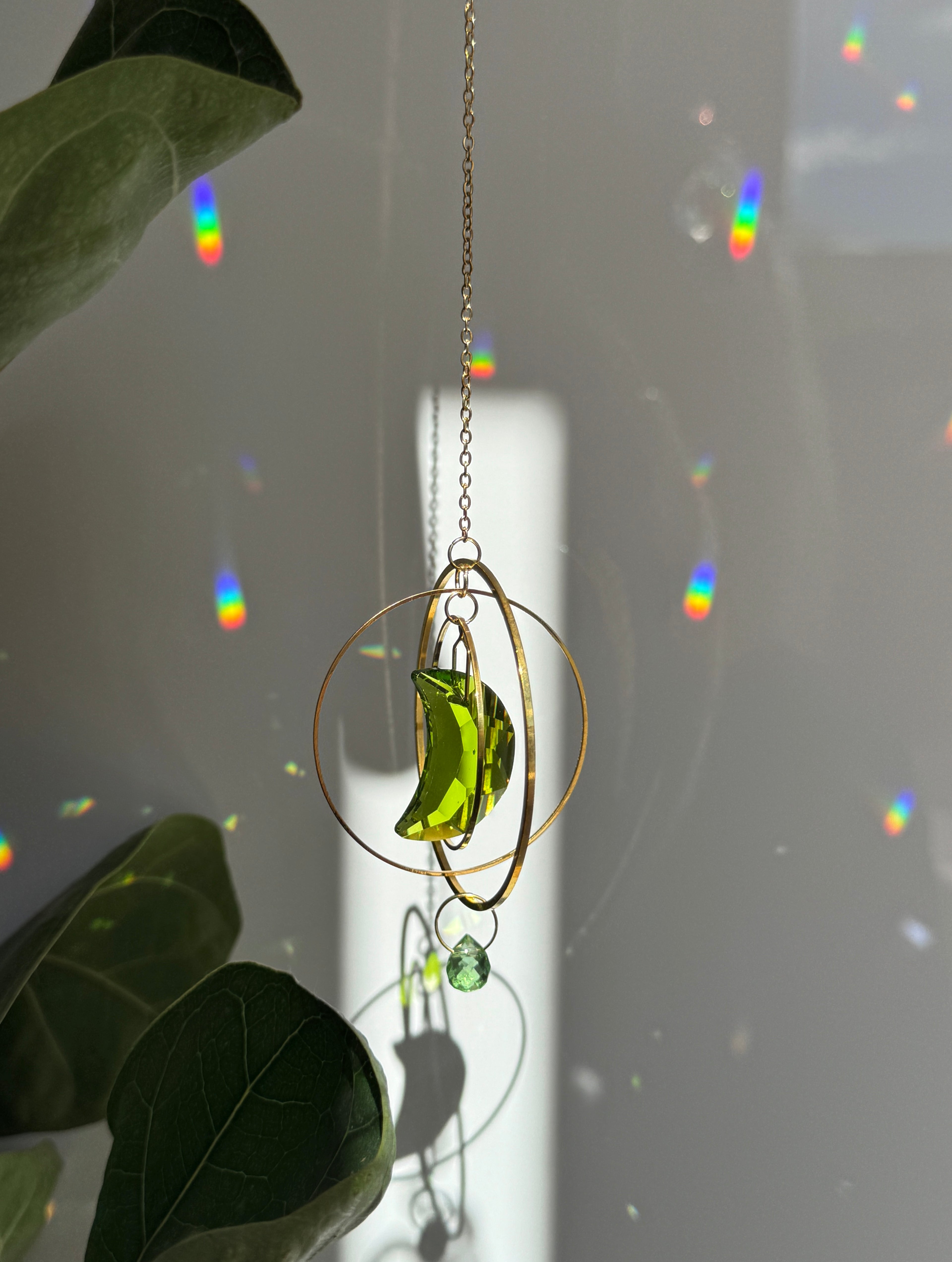 Handmade green crescent moon crystal suncatcher "Over the Moon" casting magical rainbows on a wall. Celestial gold ring window decor and rainbow maker (Sonnenfänger)