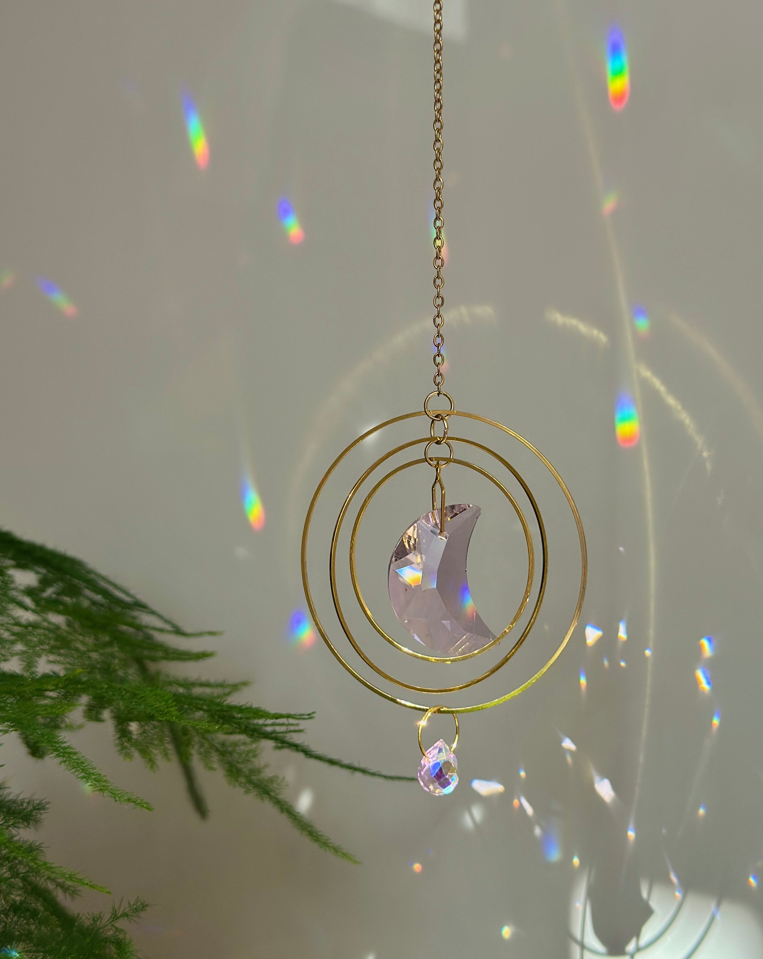 Handmade pink crescent moon suncatcher hanging in a sunny window creating rainbow prisms on the wall