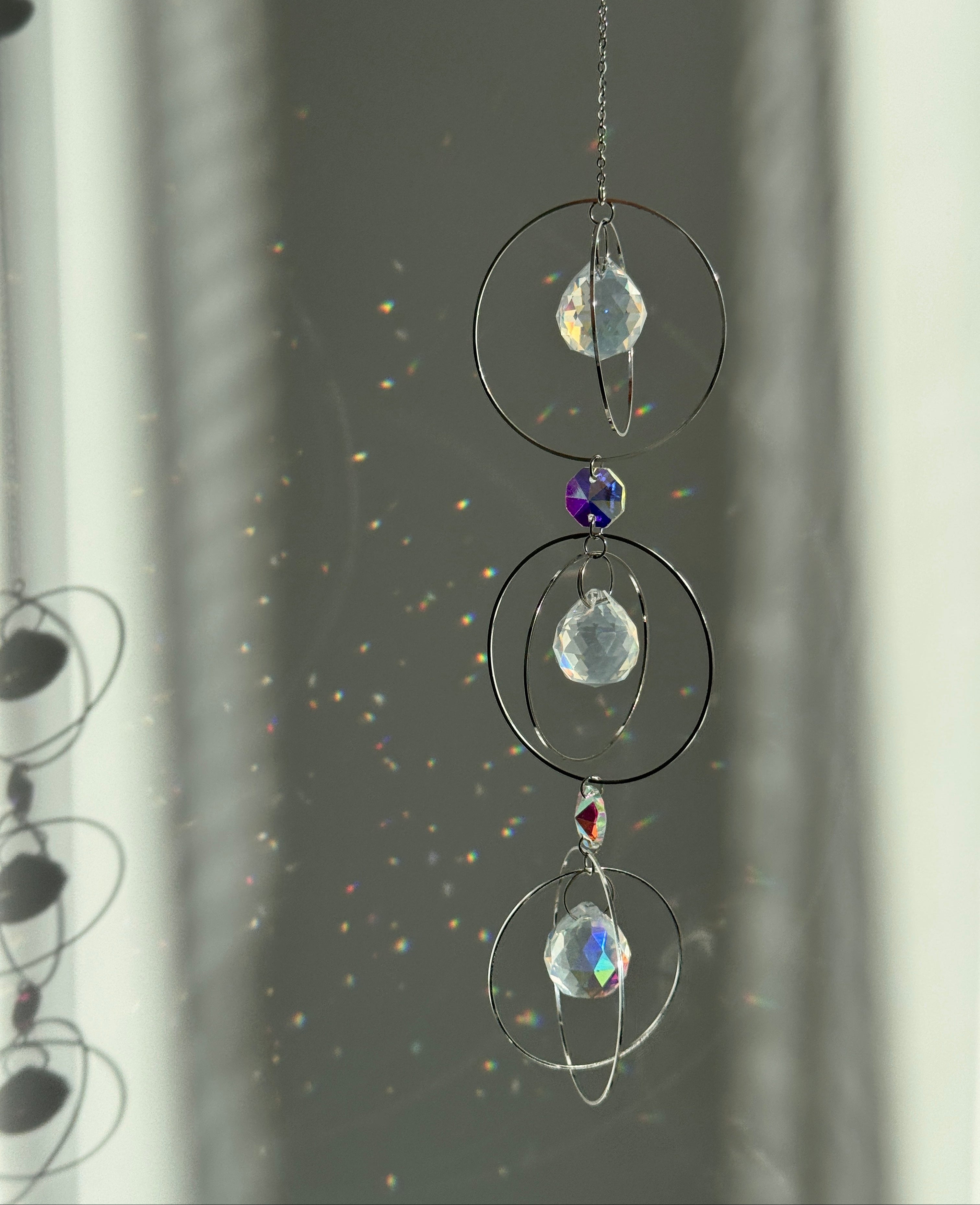 A silver-toned triple-tiered suncatcher made of stainless steel hoops. Each of the three orbits holds a clear crystal sphere with an AB coating, reflecting iridescent rainbow colors against a neutral background.