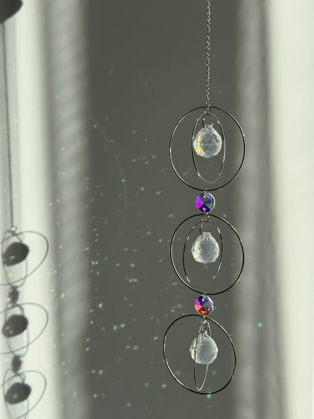 A silver-toned triple-tiered suncatcher made of stainless steel hoops. Each of the three orbits holds a clear crystal sphere with an AB coating, reflecting iridescent rainbow colors against a neutral background.
