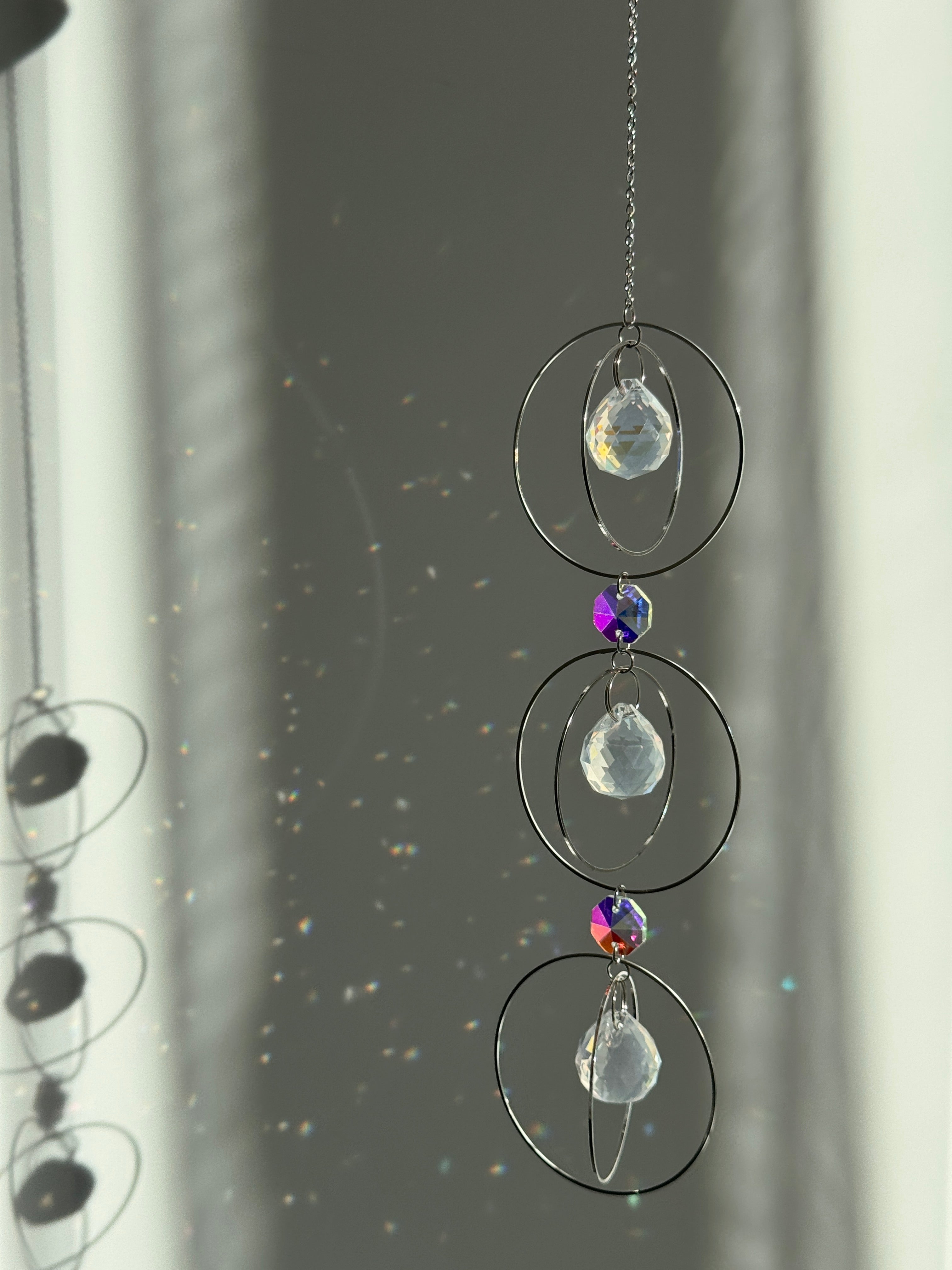 A silver-toned triple-tiered suncatcher made of stainless steel hoops. Each of the three orbits holds a clear crystal sphere with an AB coating, reflecting iridescent rainbow colors against a neutral background.