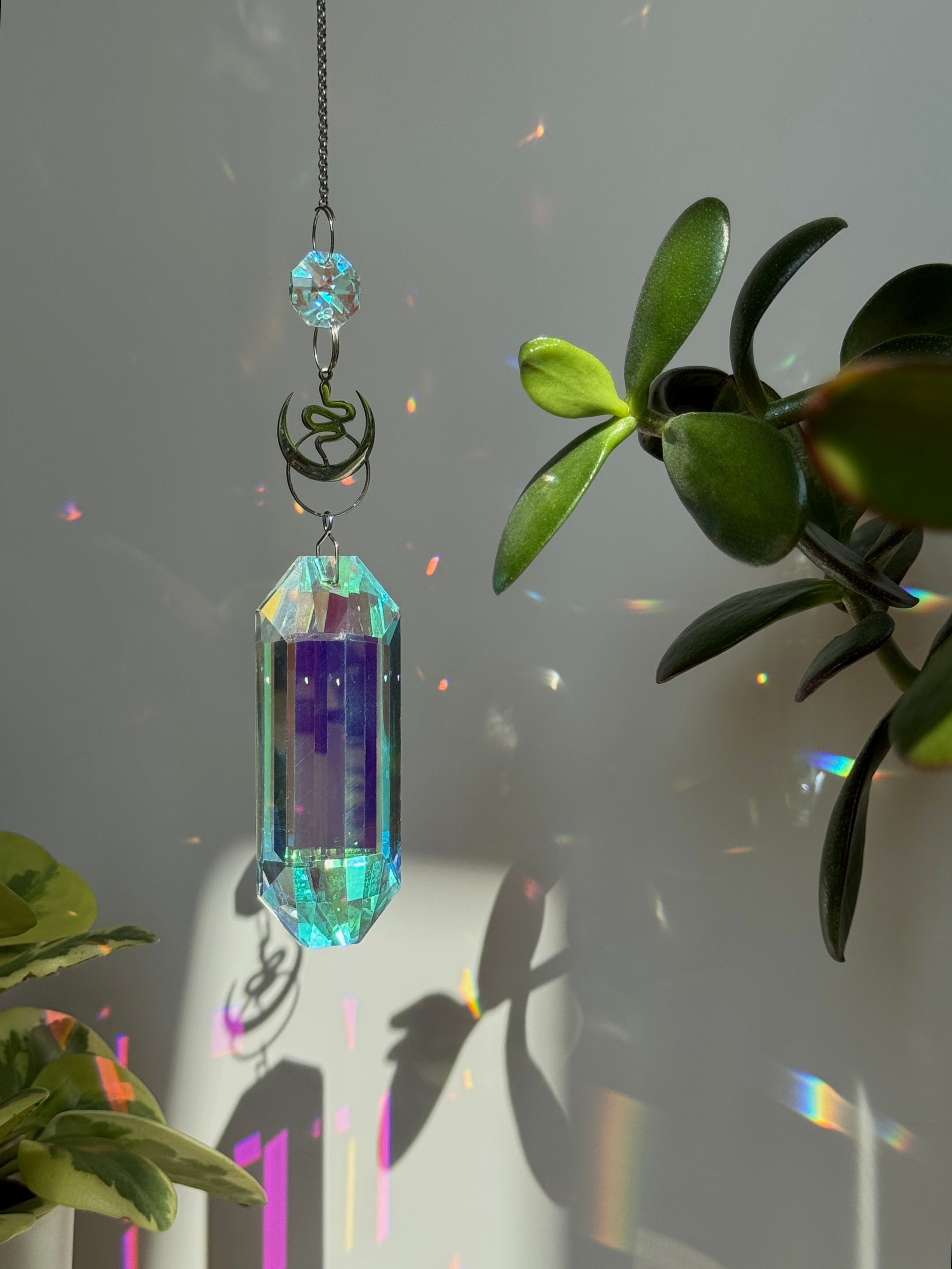 Lunar Obelisk celestial suncatcher (Sonnenfänger) featuring a gold snake charm and a large 7.5cm faceted crystal prism scattering rainbows (Regenbogen).