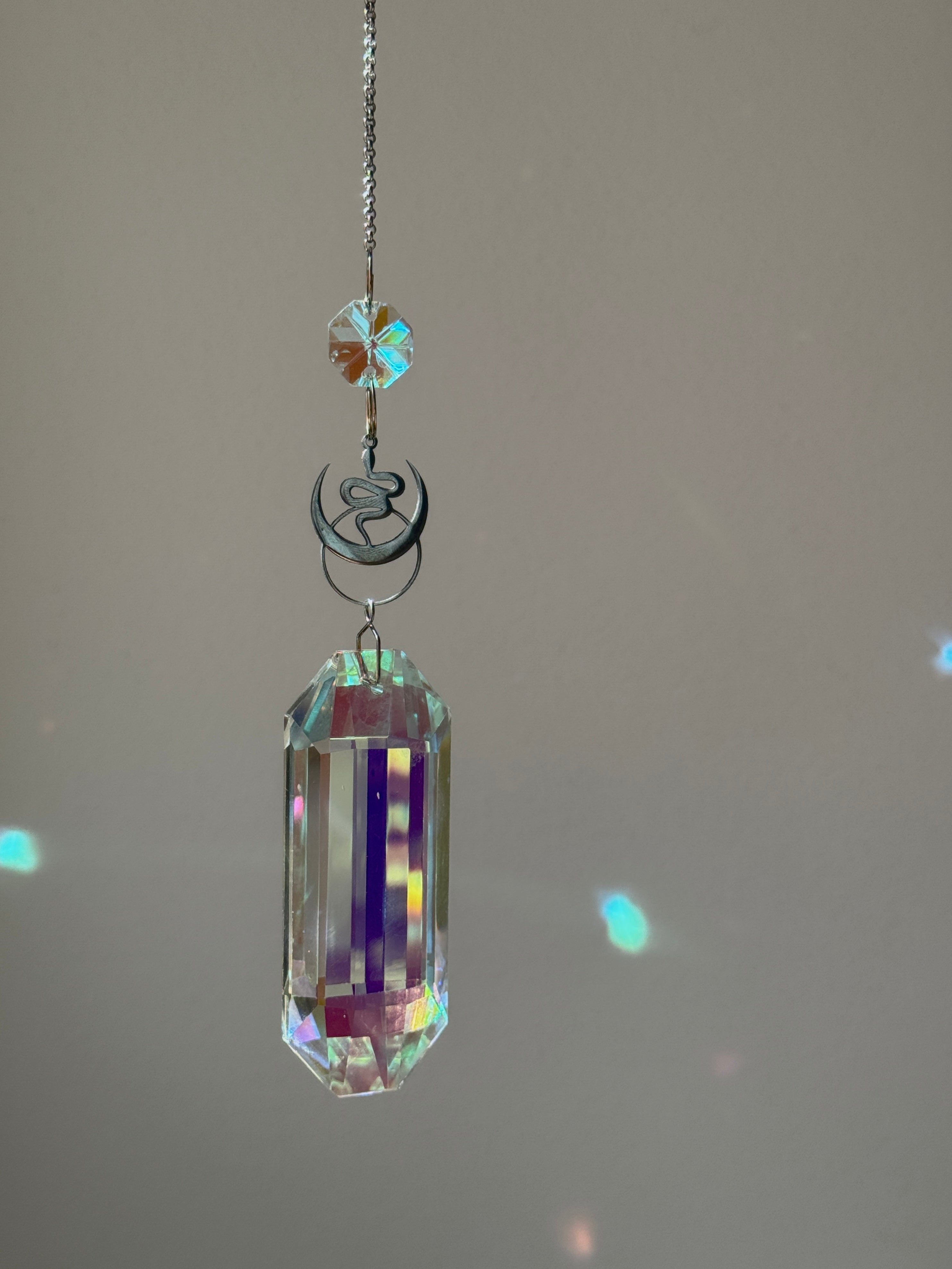 Lunar Obelisk celestial suncatcher (Sonnenfänger) featuring a gold snake charm and a large 7.5cm faceted crystal prism scattering rainbows (Regenbogen).