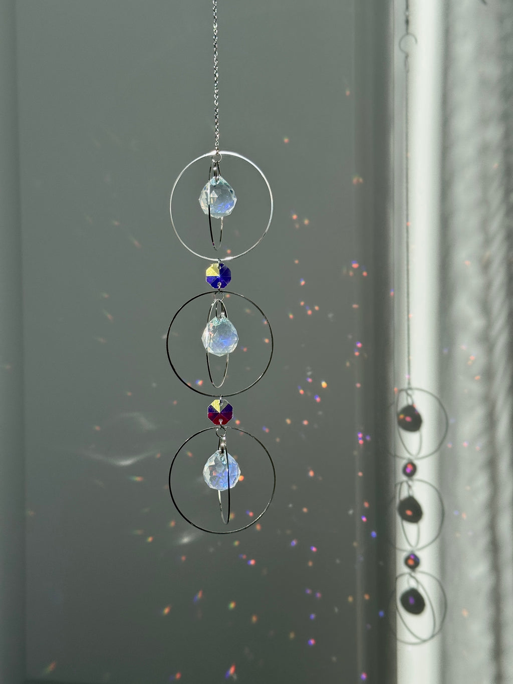 A silver-toned triple-tiered suncatcher made of stainless steel hoops. Each of the three orbits holds a clear crystal sphere with an AB coating, reflecting iridescent rainbow colors against a neutral background.