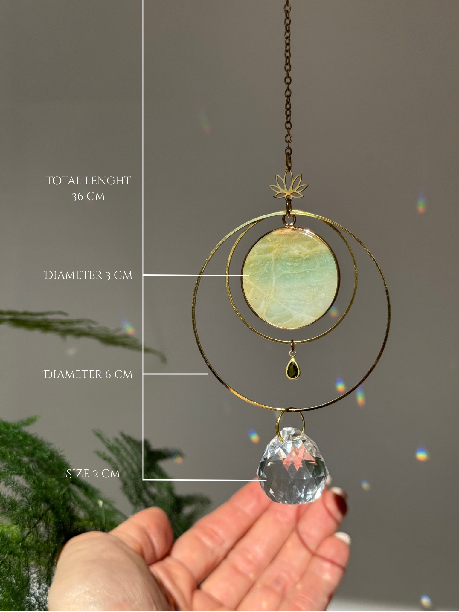 Detailed view of a gold lotus suncatcher featuring a round green Amazonite stone disc and a large faceted crystal drop reflecting rainbow light spots on a soft grey background.
