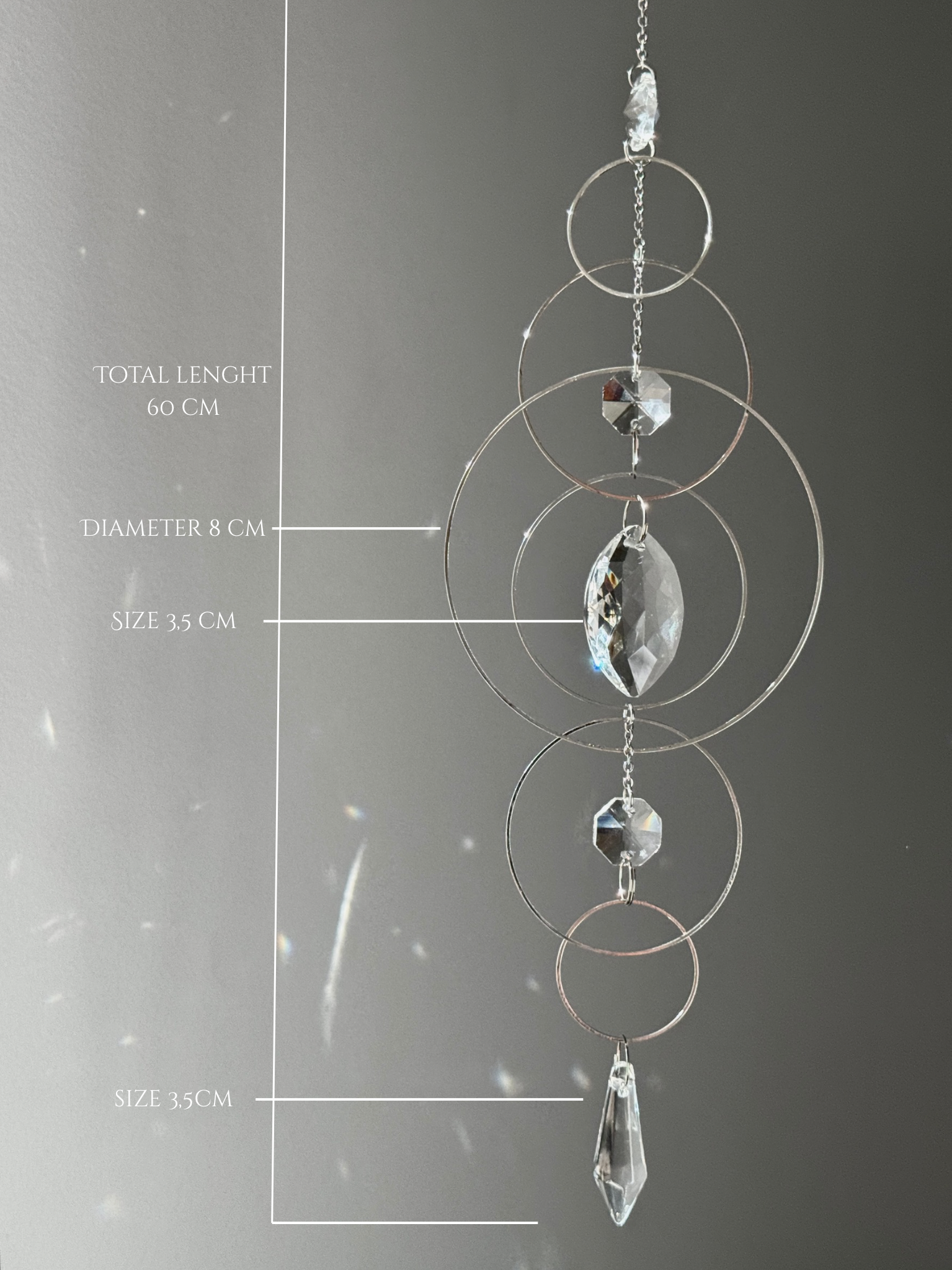 60cm silver geometric suncatcher featuring interlocking concentric hoops and clear marquise-cut crystal prisms, hanging in a window and casting rainbows on a wall.