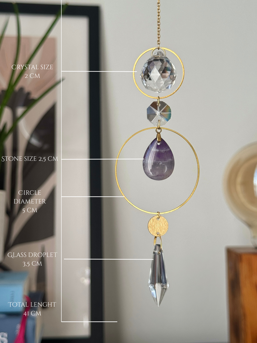 A gold suncatcher ornament with a clear crystal ball, faceted stone, purple amethyst teardrop, and glass droplet, shown with measurement labels overlaid on the left side.