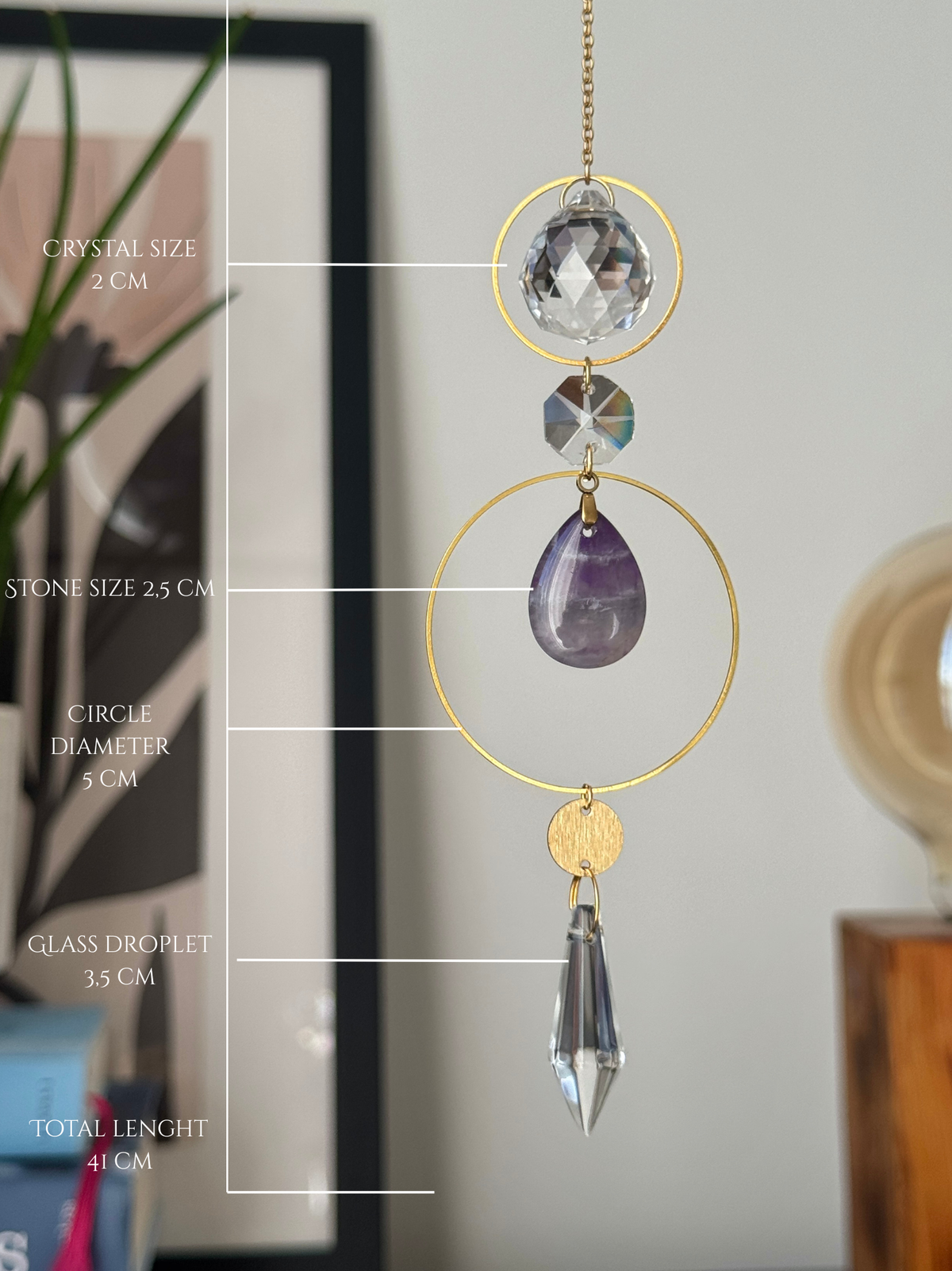 A gold suncatcher ornament with a clear crystal ball, faceted stone, purple amethyst teardrop, and glass droplet, shown with measurement labels overlaid on the left side.