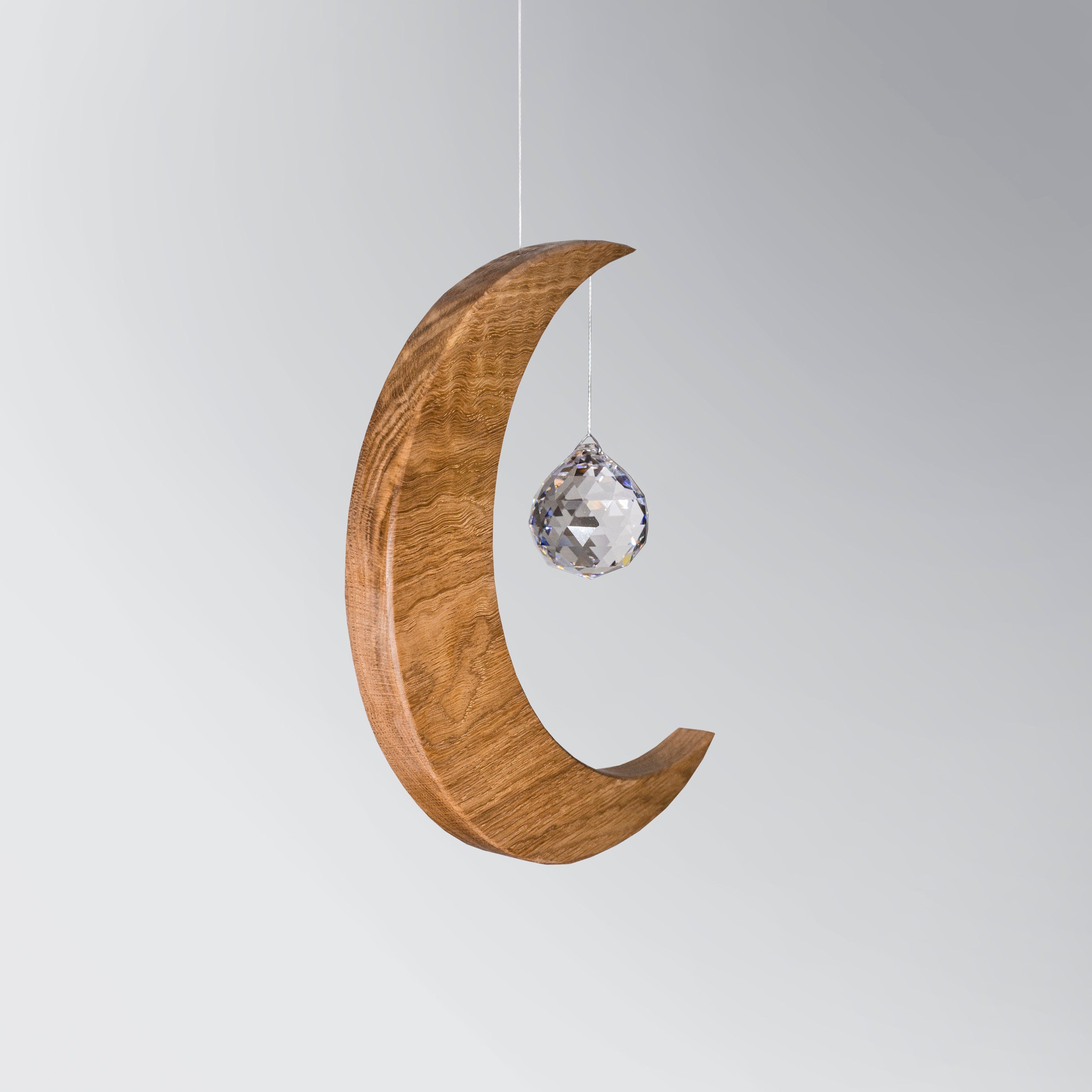 Signature Crescent Mond Sonnenfänger: Handcrafted Oak Wood Moon with 4cm Asfour Kristallprisma hanging in sunlight.