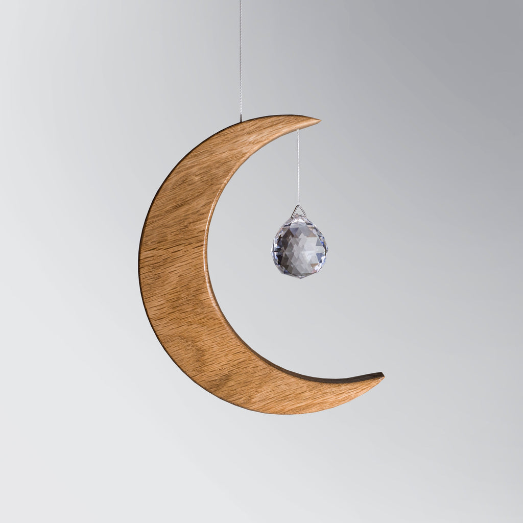 Signature Crescent Mond Sonnenfänger: Handcrafted Oak Wood Moon with 4cm Asfour Kristallprisma hanging in sunlight.