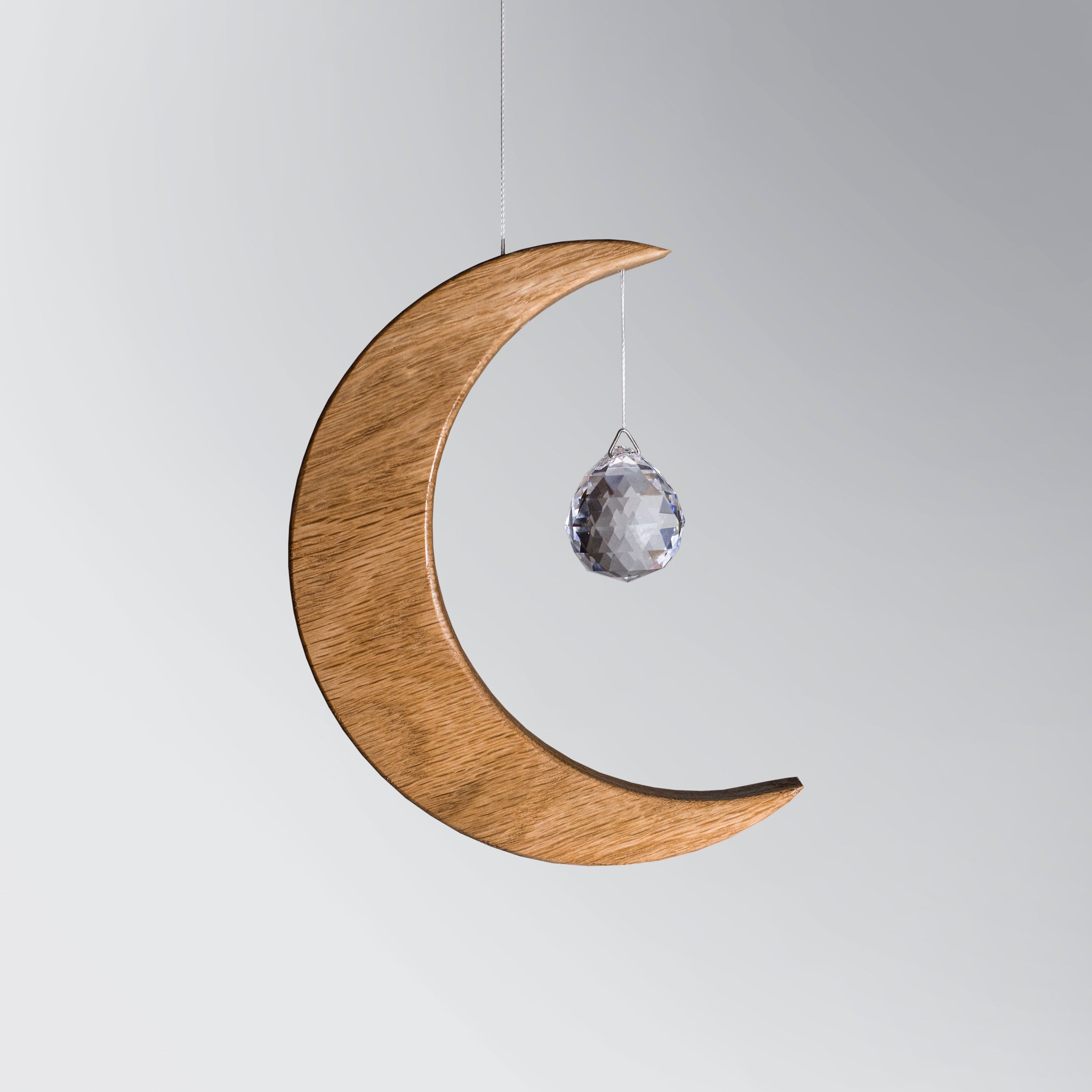 Signature Crescent Mond Sonnenfänger: Handcrafted Oak Wood Moon with 4cm Asfour Kristallprisma hanging in sunlight.