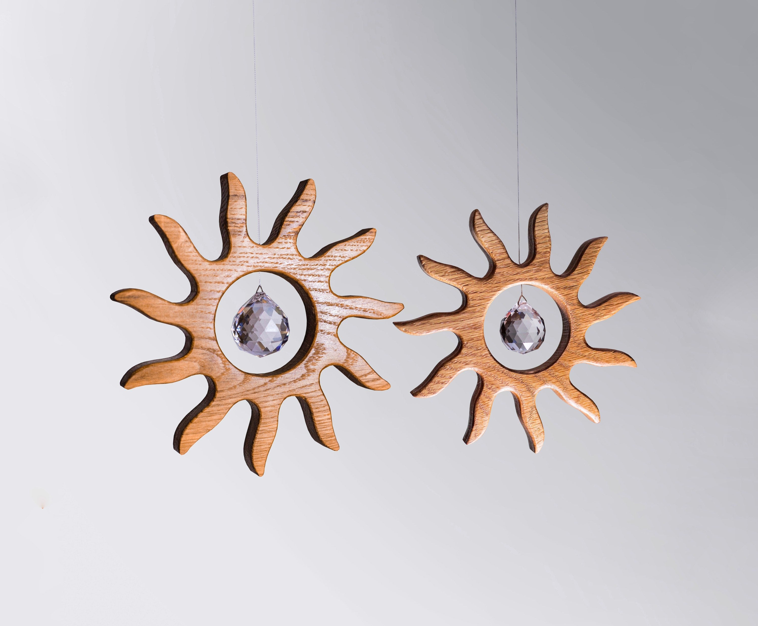 Handgefertigter Sonnenfänger aus Eichenholz (Oak) in Sonnenform with a central Asfour crystal prism. The Solstice wooden suncatcher casting rainbows on a white wall. Hochwertige Wohndekoration und Regenbogenmacher für Fenster oder Balkon.