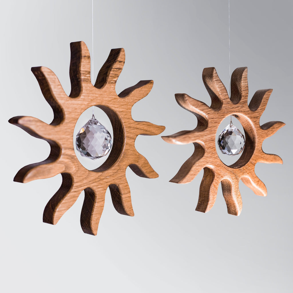 Handgefertigter Sonnenfänger aus Eichenholz (Oak) in Sonnenform with a central Asfour crystal prism. The Solstice wooden suncatcher casting rainbows on a white wall. Hochwertige Wohndekoration und Regenbogenmacher für Fenster oder Balkon.