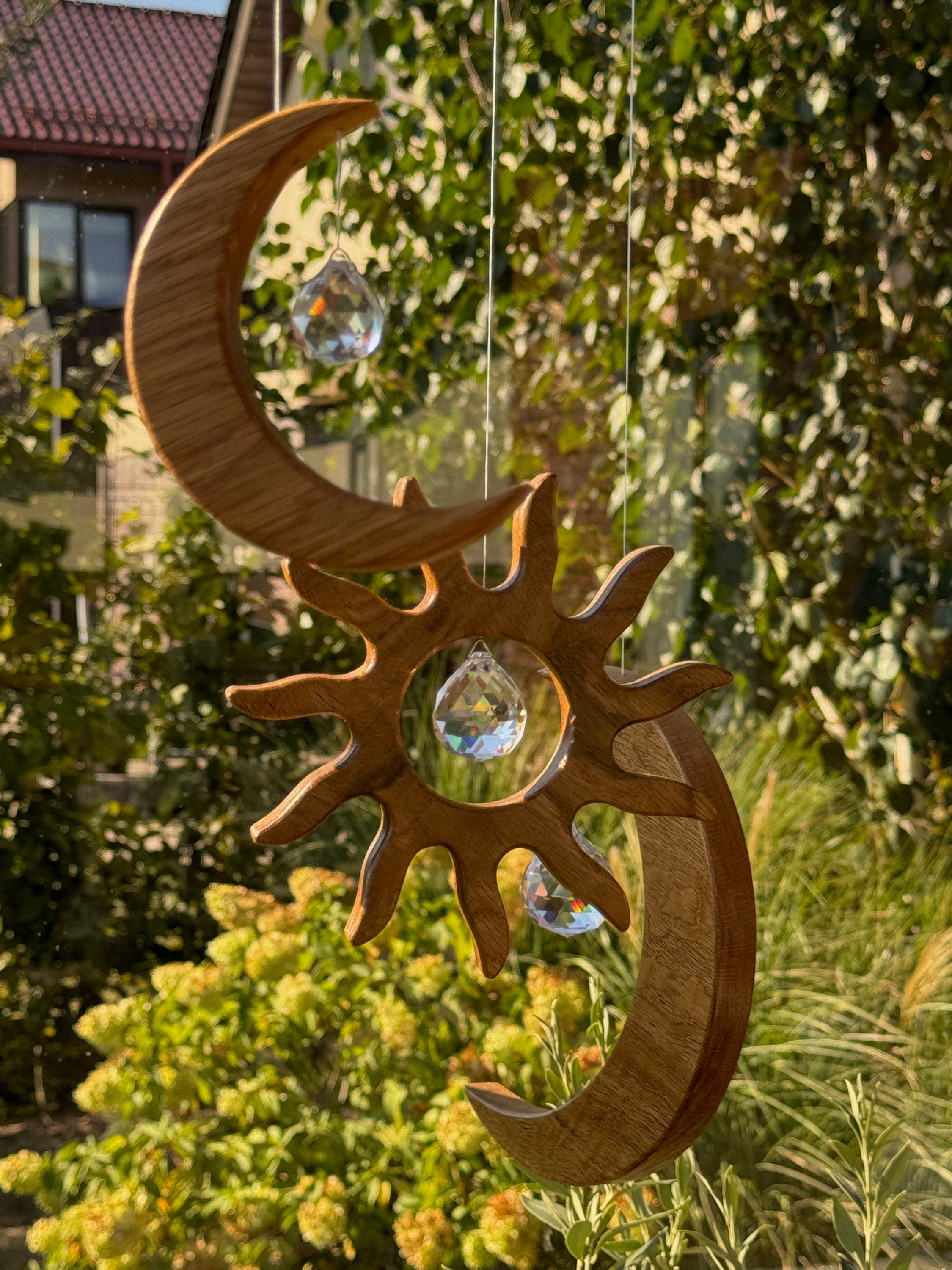 Handgefertigter Sonnenfänger aus Eichenholz (Oak) in Sonnenform with a central Asfour crystal prism. The Solstice wooden suncatcher casting rainbows on a white wall. Hochwertige Wohndekoration und Regenbogenmacher für Fenster oder Balkon.